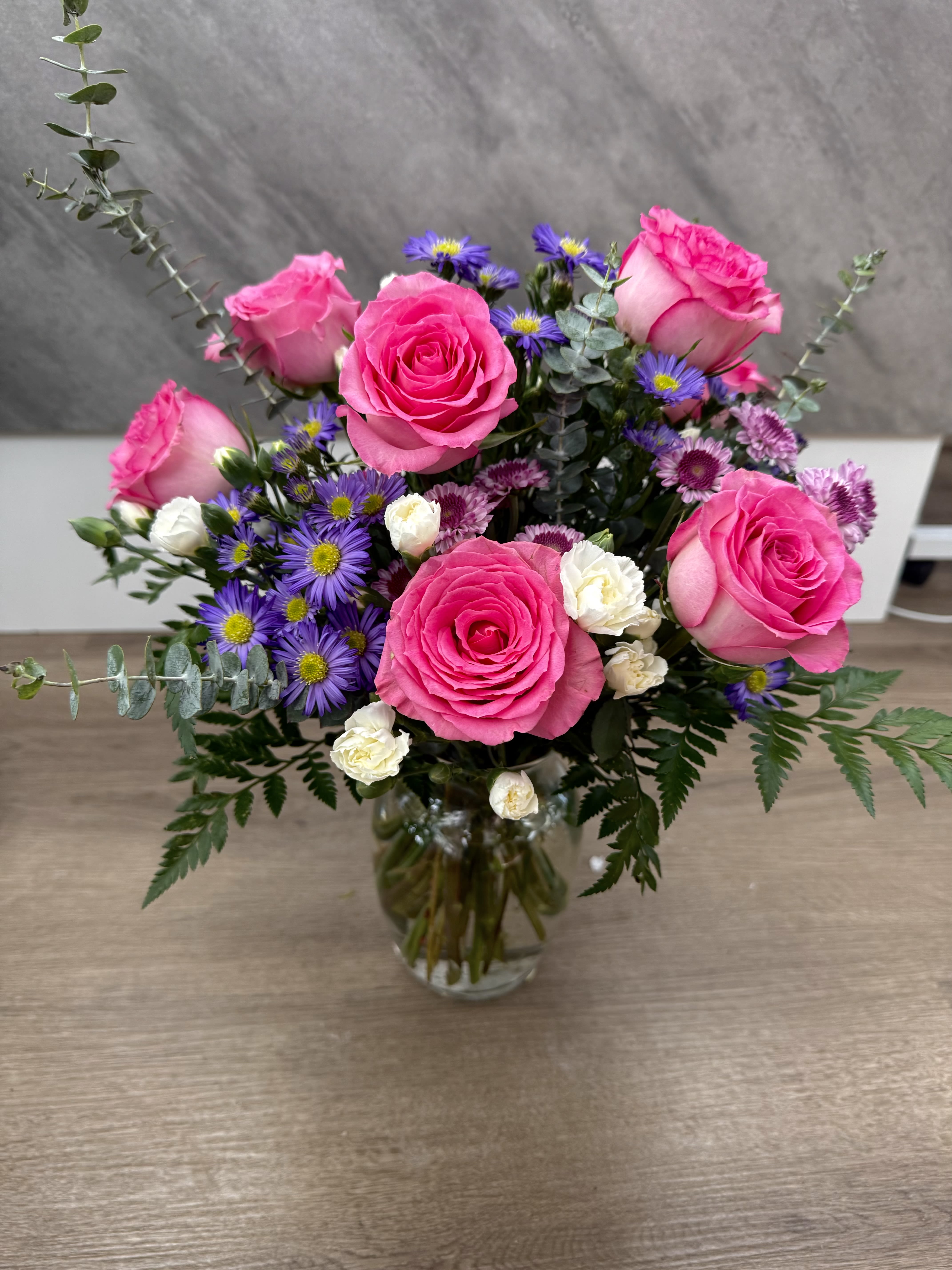 A Blushy beauty - A charming mix of pink roses accented with delicate purple blooms, creamy white florals, and fresh greenery. Designed in a clear glass vase, this arrangement is perfect for birthdays, thank-you gifts, or just because.
