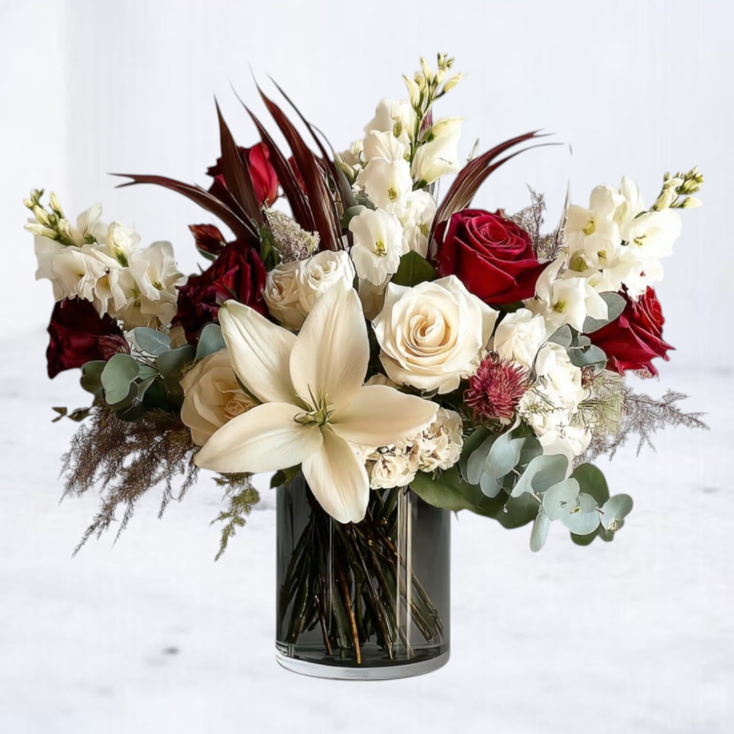 Crimson &amp; Ivory Elegance - The Crimson &amp; Ivory Elegance Bouquet is a stunning display of sophistication, blending timeless beauty with modern flair. Featuring velvety red roses, creamy white roses, elegant white lilies, and graceful stock flowers, this arrangement is accented with deep greenery, textured foliage, and dramatic touches of burgundy plumes. Designed in a sleek glass vase, it makes a breathtaking gift for anniversaries, romantic gestures, sympathy tributes, or any occasion where luxury is essential.  Available for same-day flower delivery in Galveston, Houston, and surrounding areas, this premium bouquet is the perfect choice for celebrating life’s most meaningful moments.   Substitution Disclaimer: Due to seasonal availability, some blooms may be replaced with similar varieties of equal or greater value to maintain the design’s look and integrity. Your arrangement will always reflect the same spirit, palette, and premium quality.