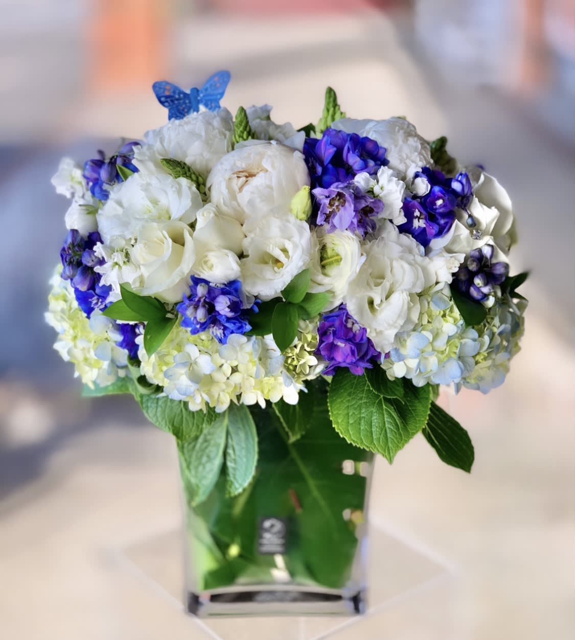 Blue Brandy - White and Blue Flowers Peonies Roses Delphinium  - For a unique essence of blue and white blooms, or to welcome in a beautiful baby boy, this design is composed of an abundance of lush white and blue blooms, including Peonies (if in season), Roses, Hydrangeas, Delphinium, and more. 