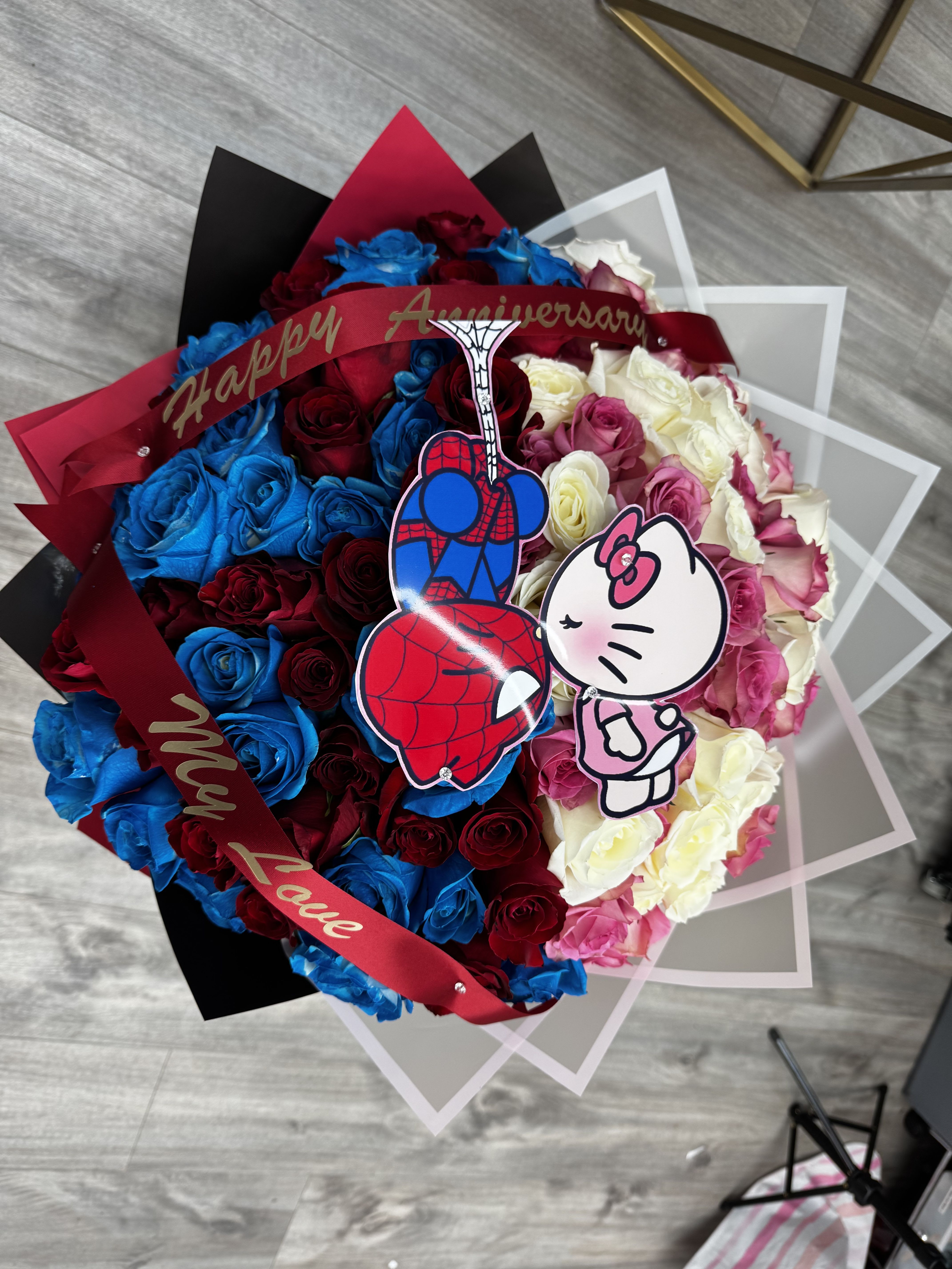 “Playful Love” – Custom Character Luxury Roses Bouquet - A fun, romantic, and unforgettable way to say I love you.  This luxury bouquet features 100 premium roses in white, blush pink, red, and hand-painted blue, designed in a bold color-block style and finished with custom character toppers and a personalized ribbon.  Only the blue roses are hand-painted, adding a unique artisanal touch. The character details make this arrangement perfect for playful couples, birthdays, and Valentine’s Day gifts that stand out and spark instant smiles.  ️ 100 premium roses (white, blush pink, red &amp; hand-painted blue) ️ Hand-painted blue roses ️ Gypsophila (baby’s breath) ️ Luxury wrapping ️ Custom character toppers included ️ Personalized ribbon included ️ One-of-a-kind handcrafted design