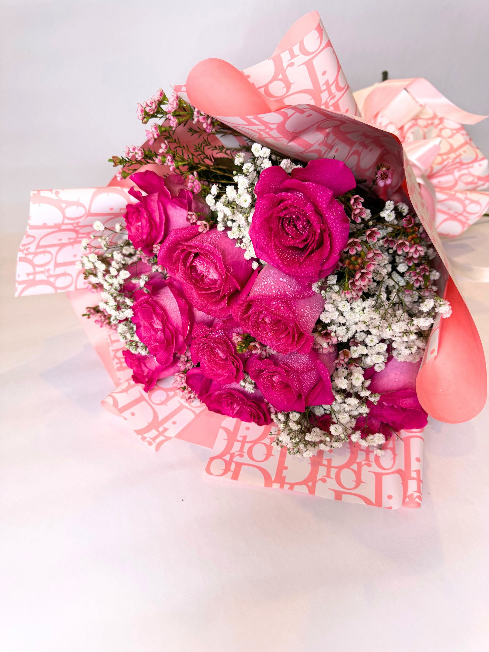 XOXO Pink Roses - At the center is a lush bouquet of one dozen pink roses, each bloom full and velvety, symbolizing love and passion. The roses are tightly arranged to create a rich, rounded shape, with fresh green foliage peeking through for contrast. They’re wrapped in elegant paper, finished with a satin red ribbon for that timeless Valentine’s touch. Other color paper options available please call or message.  The whole arrangement gives off a “wow” moment—romantic, thoughtful, and heartfelt—perfect for saying I love you in a way that feels both meaningful and memorable. 