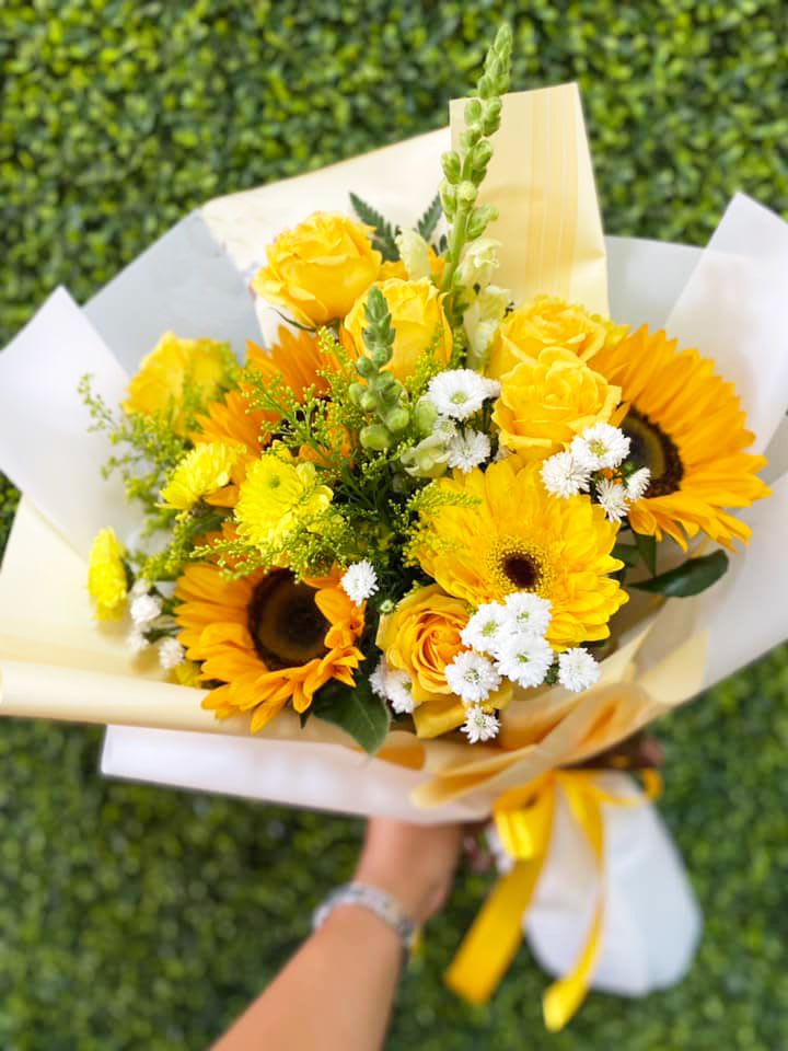 Golden Sunshine Bouquet - The Golden Sunshine Bouquet a beautiful yellow bouquet of Sunflowers, Geberas Daisies, Snapdragons, Yellow Cushion and White Poms with accents of Solidago. 