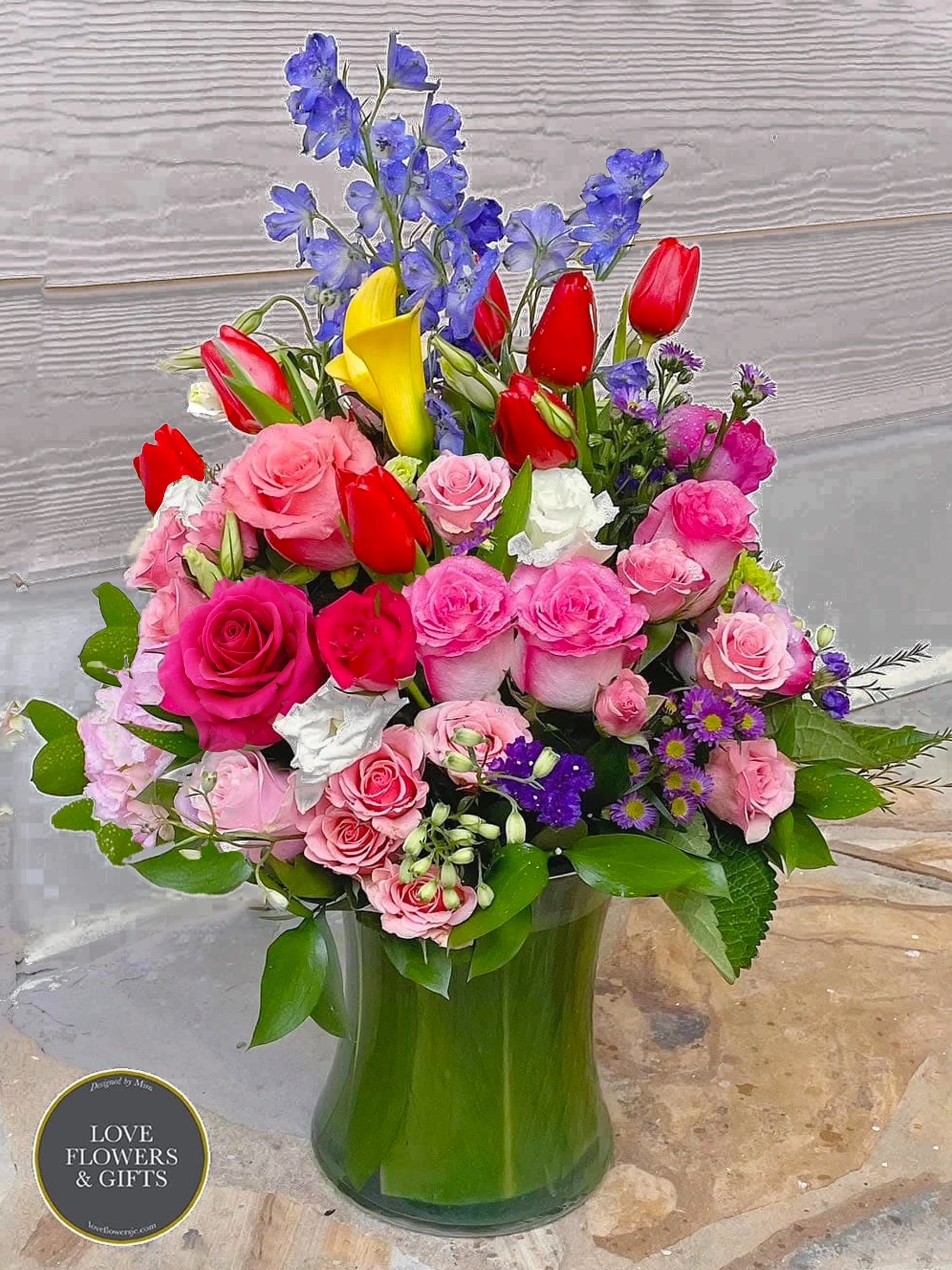 Perfectly Splendid - Send an unforgettable experience with this splendid and abundant arrangement. Designed in a high-quality glass vase, wrapped with banana and dracaena leaves, made with assorted roses, calla liles, tulips, and other flowers in round-style.   Enjoy equally from all angles, 360 degrees.   