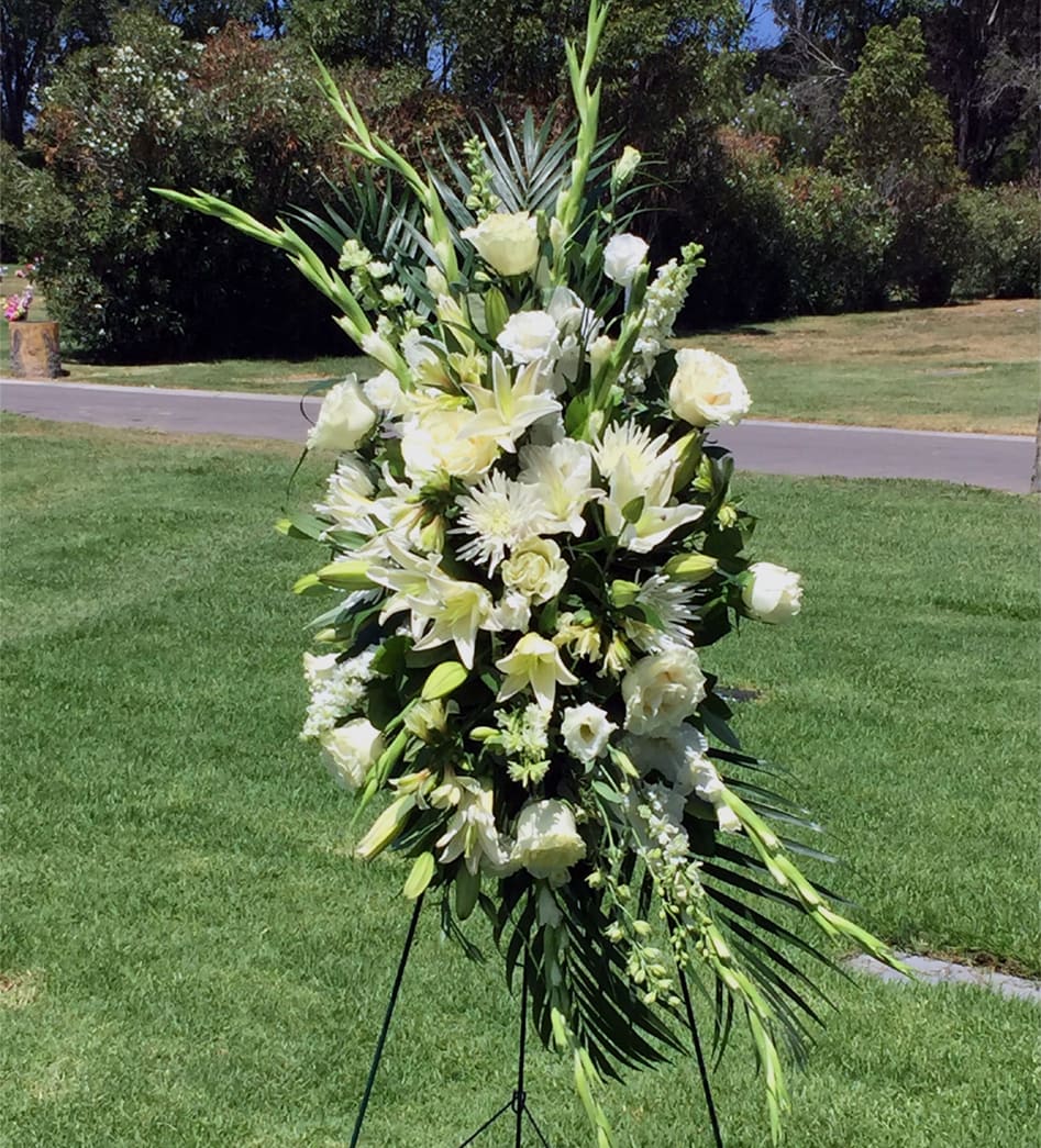 All White Sympathy Standing Spray - Send your deepest wishes of sympathy in an elegant and beautiful way with our all-white standing spray, crafted on an easel stand using the freshest available Roses, Lilies, Mums, Lisianthus, Gladiolus, Alstroemeria, Larkspur and more.  Our all white sympathy standing spray is appropriate for wakes, funerals, and memorial services. The flowers measure approximately 25in (W) x 50in (H), for a total of approximately 80 inches (H) when displayed on the easel stand. Deluxe and Premium designs are larger and feature more premium blooms.  Please Note: This is a special order floral arrangement. Place your order online and allow at least 1-2 business days for order processing. Please give us a call at 619-237-8842 for same day delivery options. Some substitutions may be necessary due to seasonal availability of certain blooms used in this composition. We can assure you that your order will only be upgraded with same or higher value premium blooms if a substitution is unavoidable.
