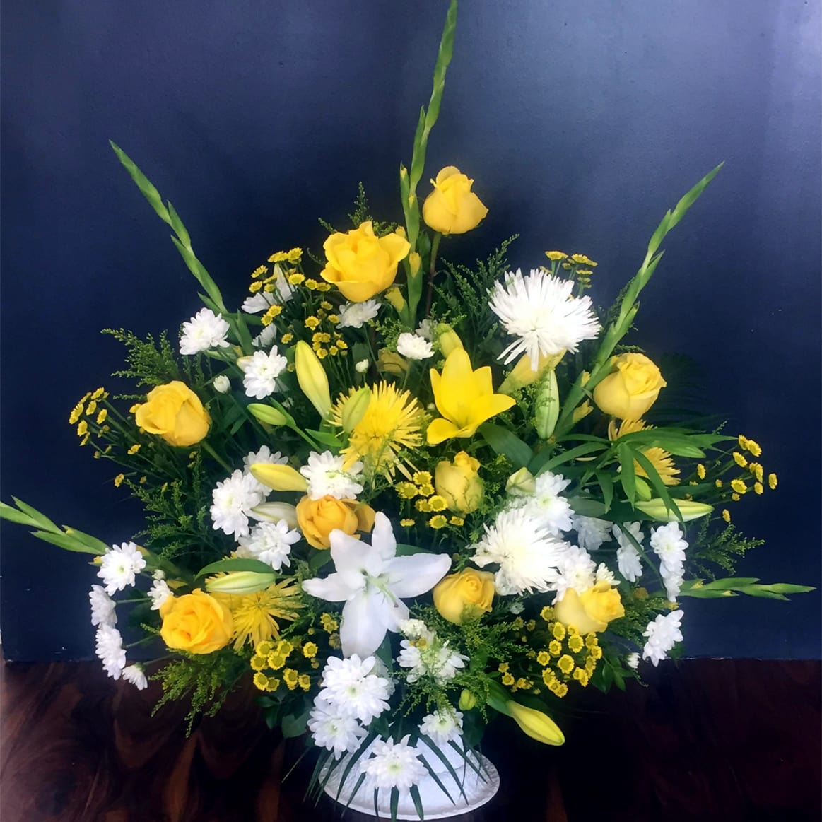 Yellow and White Sympathy Basket - Let your friends or family members know just how much you care, with our beautiful yellow and white sympathy basket. Hand-selected arrangement of the freshest Roses, Gladiolas, Lilies, Chrysanthemums, Daisies and more. Our designers hand-arrange each basket.  This one-sided design is suitable to send to a residence, a funeral home or service. Take advantage of our arrangement size upgrade options. Standard size is approximately 28" (W) x 36" (H). Deluxe and Premium versions are larger and have more premium blooms.
