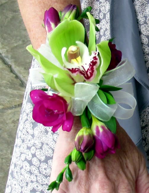 Orchid and Freesia Corsage (Wristlet) - A combination of Cymbidium Orchid and Freesia against shiny green leaves in this exclusive design.  Our wristlet corsages are perfect for any wedding, prom or special event. All of our corsages are handmade to order and can match any dress color and style. Feel free to call us at 619-237-8842 to discuss your options.