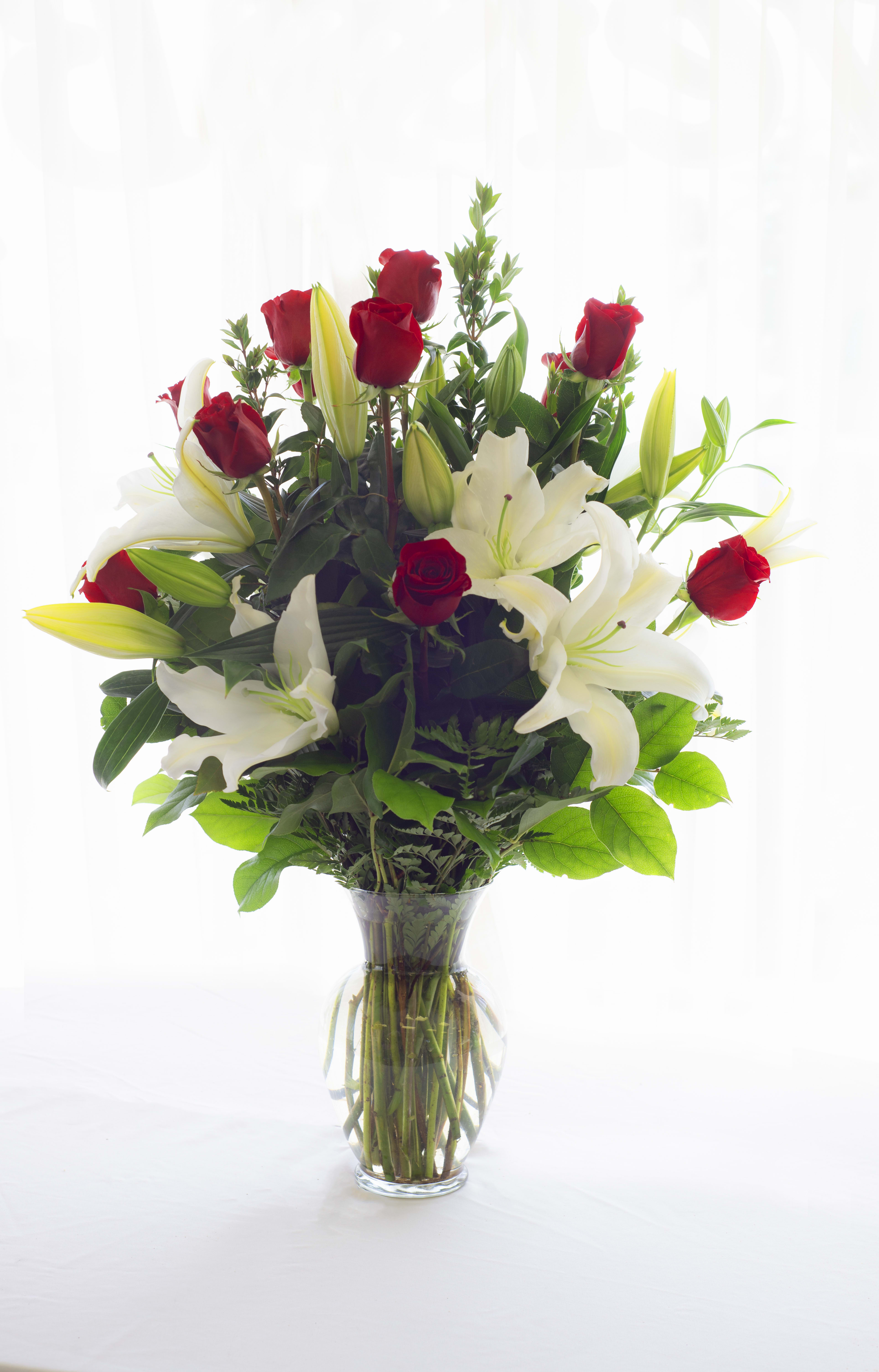 Roses and Lilies Grand - 12 long stem roses with beautiful white Asiatic Lilies with greens in a clear glass vase.
