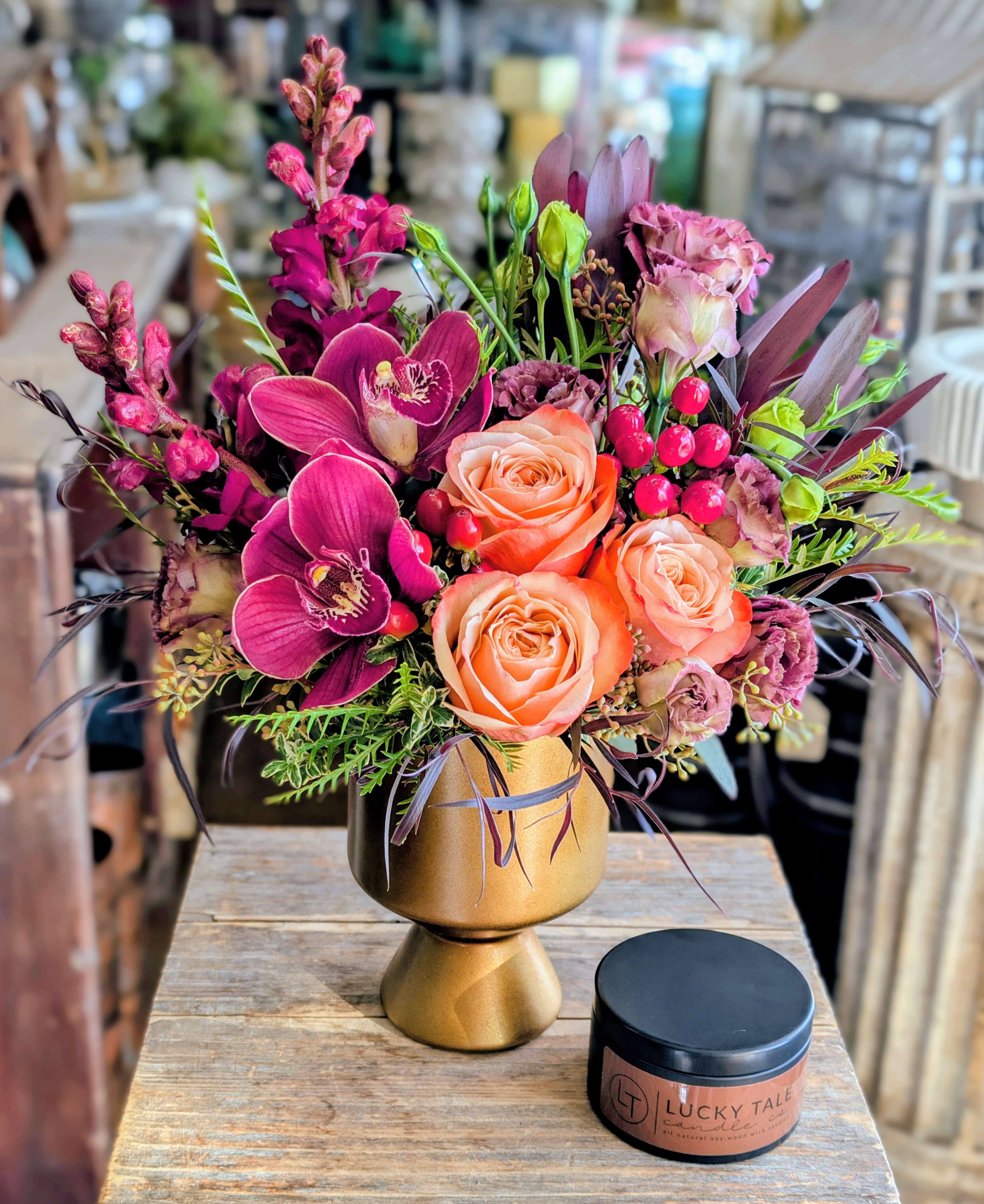 Brûlée- With A Cedar Mountain Whiskey And Coffee Candle - Introducing Brûlée, a warm and luxurious floral creation from Windmill Floral Expressions. This handcrafted arrangement blends glowing peach roses, velvety plum orchids, rich berry accents, and sculptural greenery—artfully gathered in a modern matte-gold pedestal vase. Inspired by the rich, caramelized tones of its namesake, Brûlée brings an elevated warmth and soft sophistication to any space. Paired with a decadent Cedar Mountain Whiskey and Coffee candle fragrance candle, this design becomes a full sensory experience—where the aroma of Irish coffee drifts through the room, perfectly complementing the arrangement’s rich jewel-tone palette. Thoughtful, modern, and indulgent, Brûlée makes an exceptional gift for the holidays, celebrations, or simply elevating your everyday home ambiance. Windmill Floral Expressions specializes in bespoke floral art, permanent botanicals, and mystical gifts—proudly delivering throughout Las Vegas, Henderson, Anthem, Inspirada, Seven Hills, and surrounding communities.   