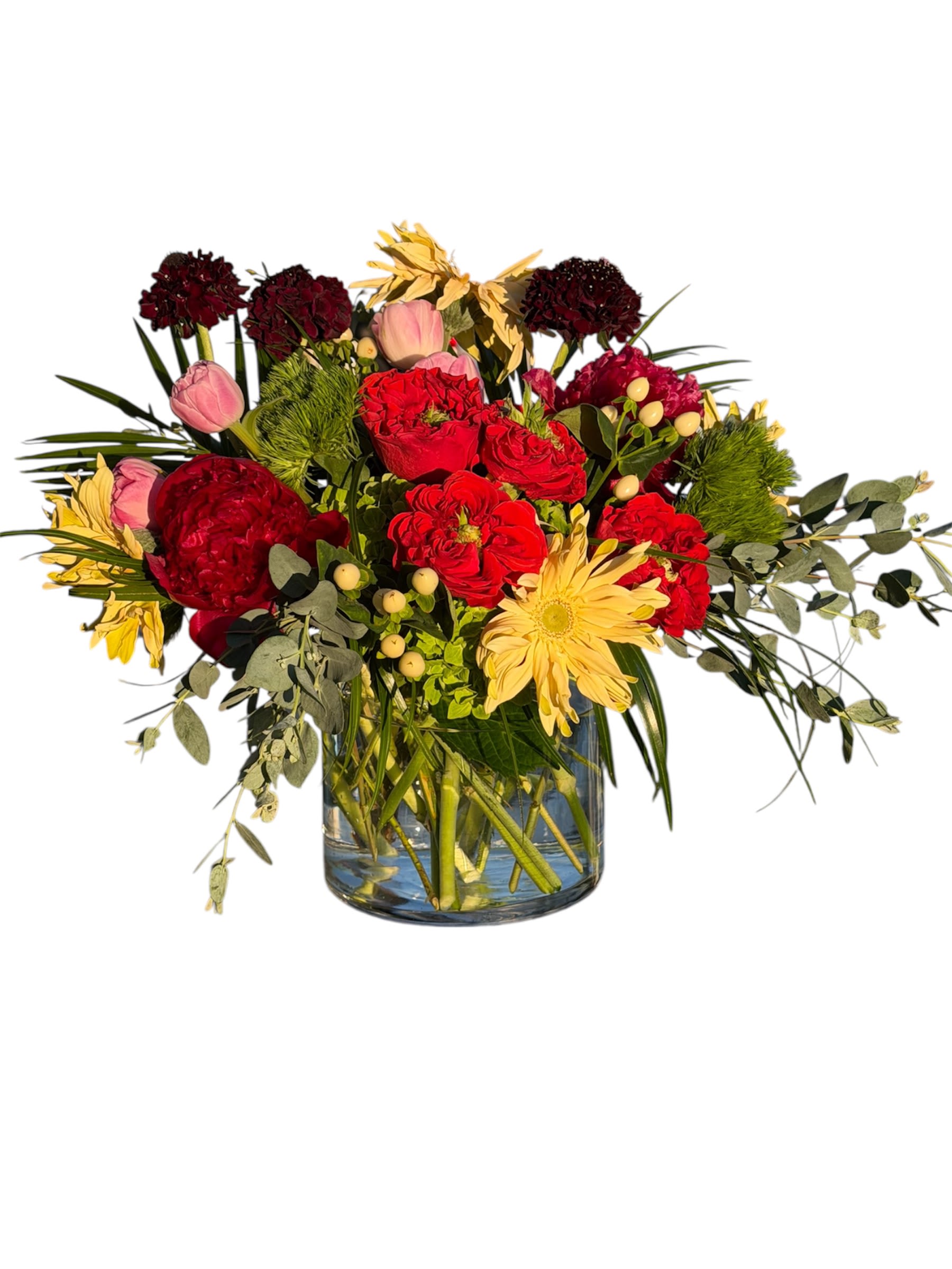 LOVE IN FULL BLOOM - A rich Valentine’s mix featuring red roses, burgundy peonies, green dianthus, ivory gerbera, green hydrangeas, burgundy scabiosa, pink tulips, and white hypericum, all gathered with fresh mixed greenery in a clear cylinder glass vase. 