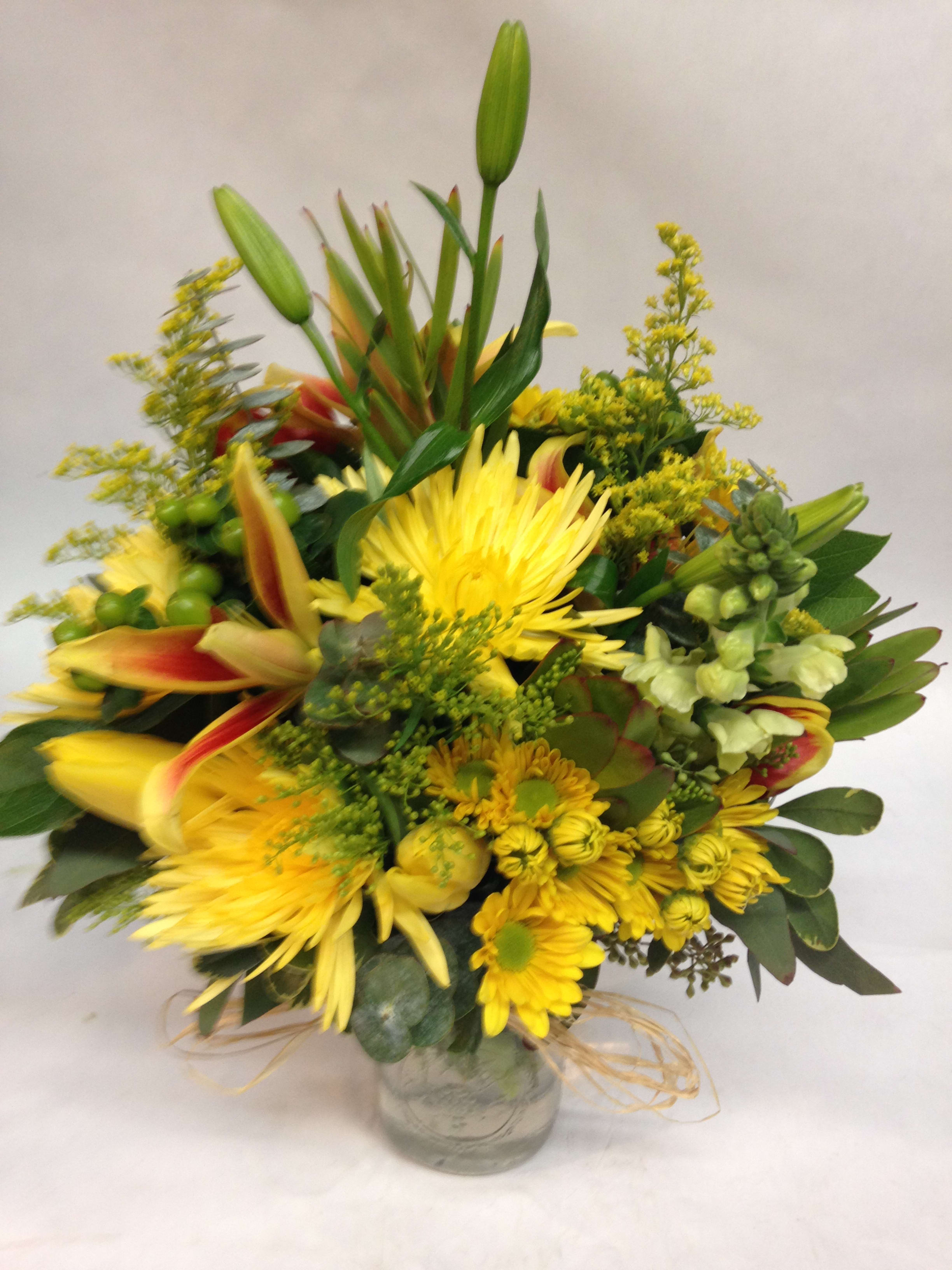 Sunny Springtime Glow. - Brighten the room with this sunny arrangement of yellow mums ,tulips, lilies, stock, solidago, and mixed filler. (Some flowers may be subject to change depending on the season. We will contact you with available flower substitutions; please contact us with specific questions if you are concerned with flower availability, thanks!)  Featured Arrangement: $100.00 