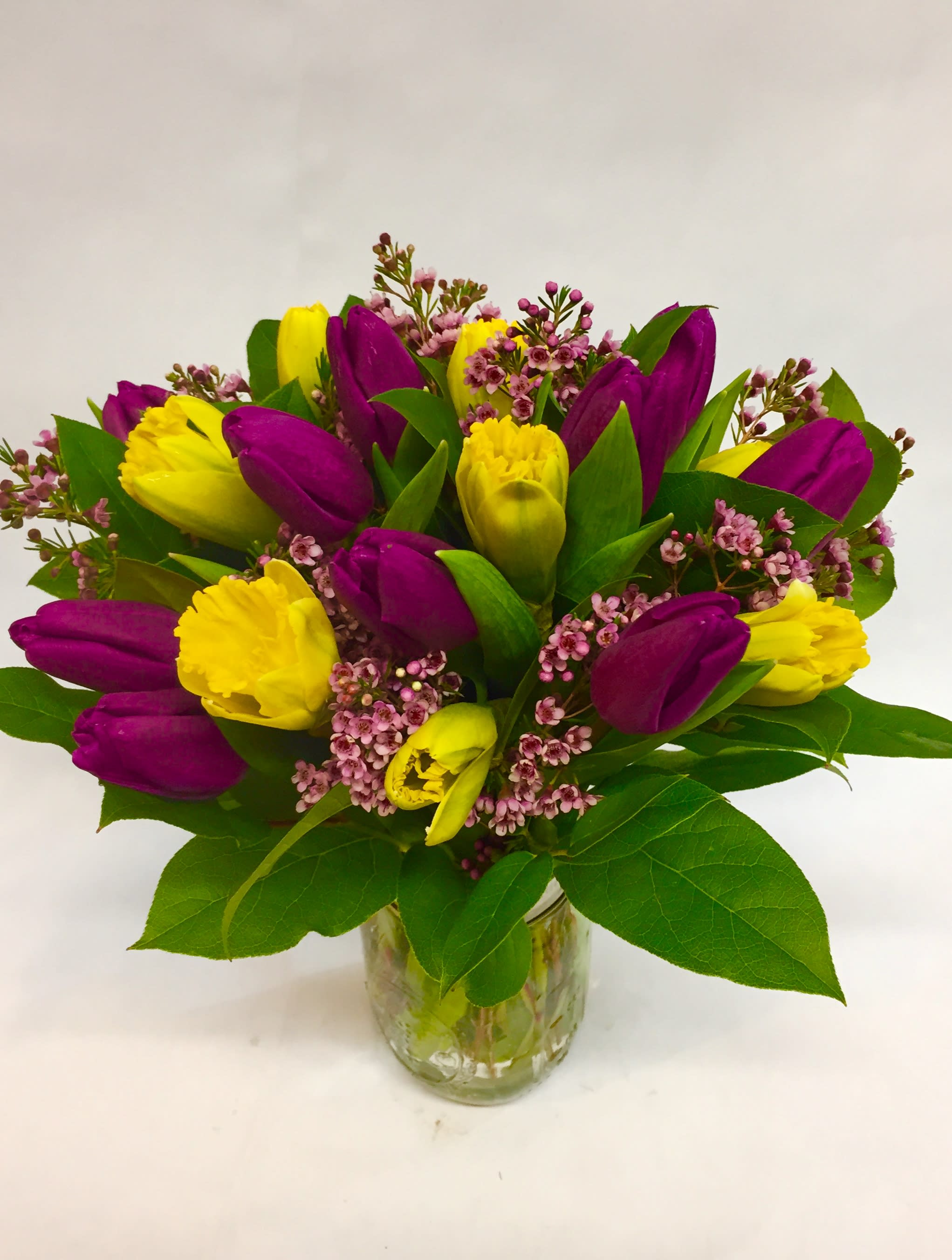 Burst of Spring - This darling jar is Spring's essence: bright daffodils (seasonal) and tulips with wax flower filler. Flowers are subject to change depending on seasonal availability. (Featured Arrangement: $75.50 Regular Price)