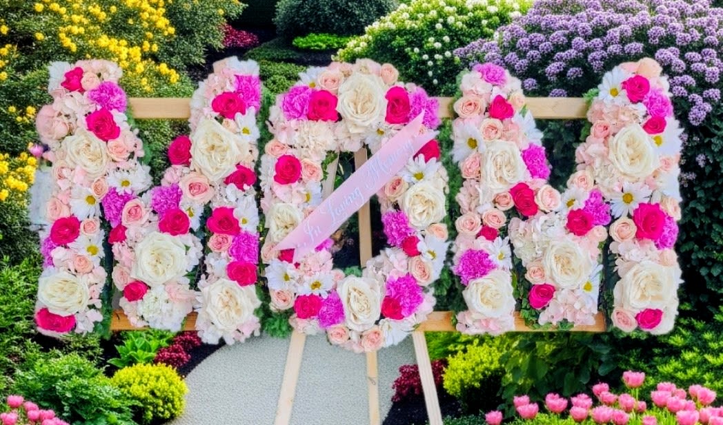 MOM Standing Sympathy Words - MOM measures 42"x18" and stands on a 5ft tall easel. Designed with in a pink mix variety and white. It has regular roses, baby roses,  carnations, mini cams, daisies and hydrangea. This can come in other colors. 