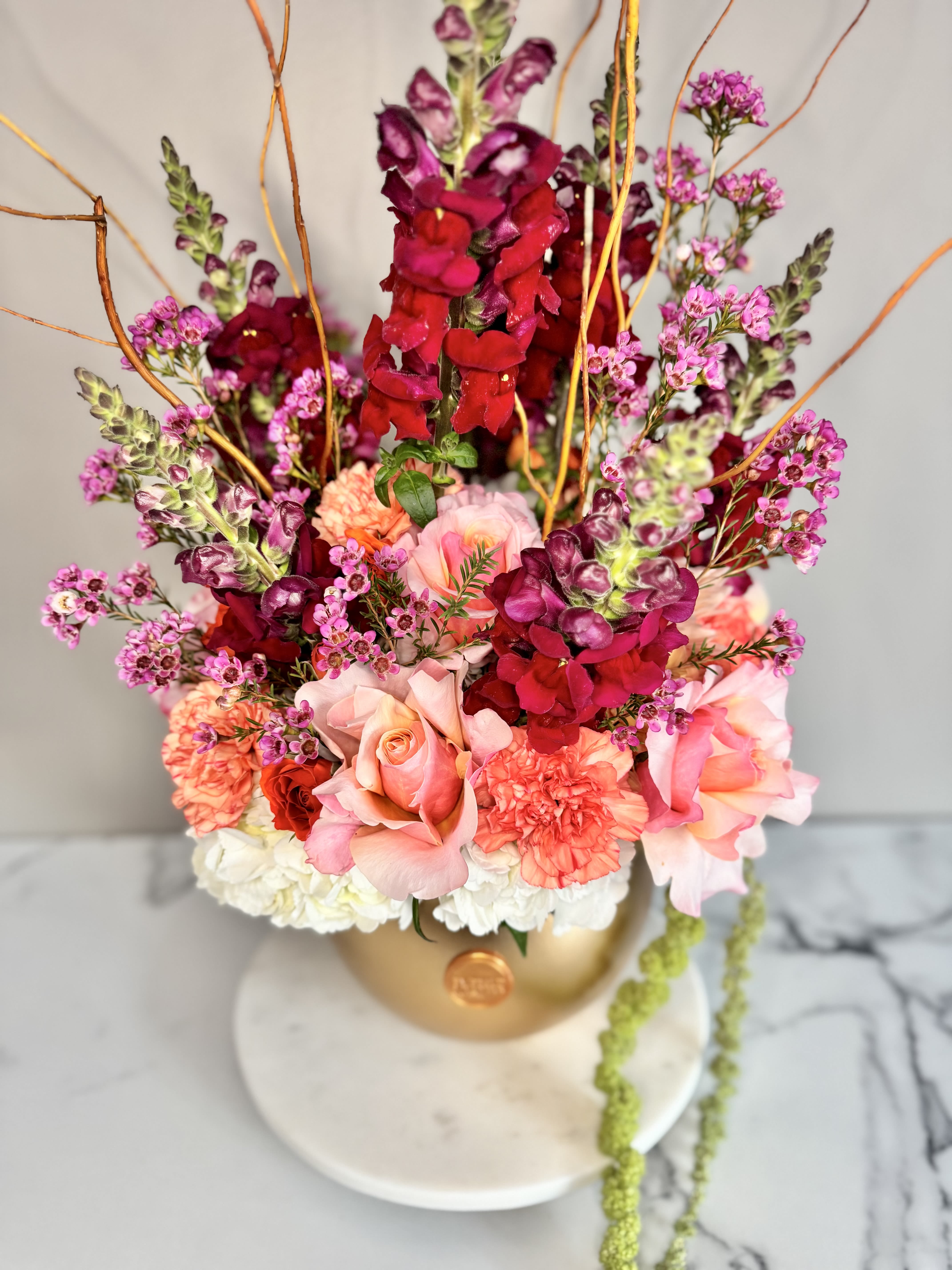 Golden Bloom Grandeur - Make a statement with Golden Bloom Grandeur, a lavish floral arrangement designed to turn heads. Curated by the florist, this stunning display features the freshest seasonal blooms arranged in an opulent gold vase, with a carefully selected color palette to suit the occasion. Lush textures, artistic accents, and striking floral combinations make it the perfect choice for grand celebrations, an elegant gift, or a showpiece for an opening night. Whether adorning a special event or elevating a space, this breathtaking arrangement exudes sophistication and charm.