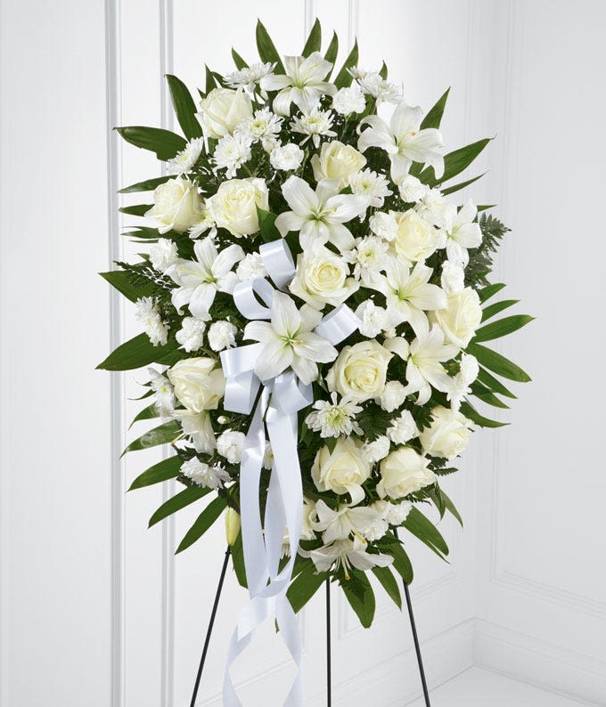 Heaven's Grace - A serene standing arrangement of white lilies, roses, snapdragons, and lush greenery. Designed with elegance and reverence, this large pedestal honors a life with purity, peace, and grace.
