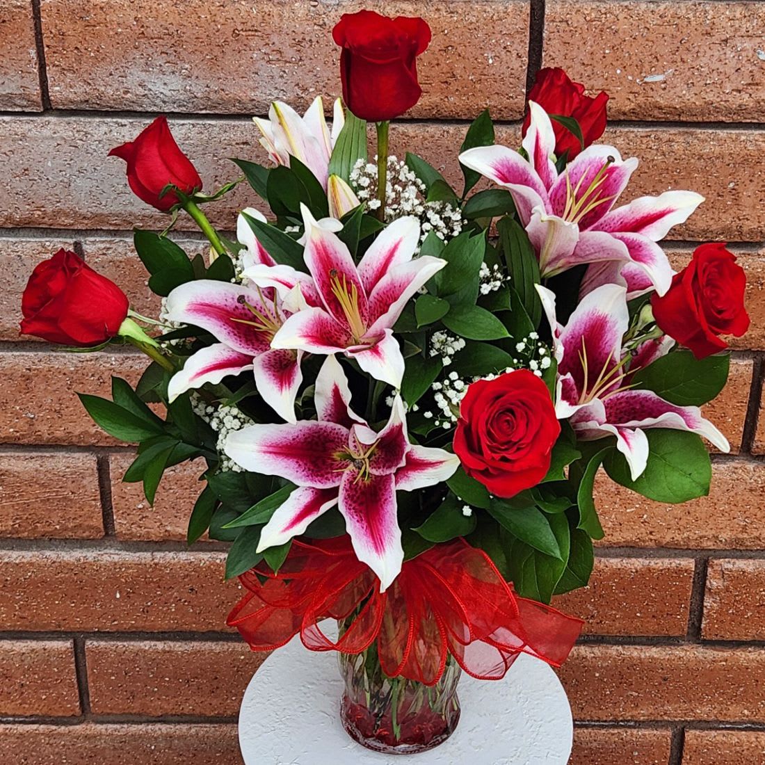 Pink Stargazer Lilies &amp; Red Rose Romance - Pink Stargazer Lilies &amp; Red Rose Romance  Celebrate life’s most meaningful moments with a breathtaking blend of fragrance, elegance, and timeless beauty. This romantic arrangement pairs fragrant Pink Stargazer Lilies with luxurious Ecuadorian long stem Red Roses, creating a classic expression of love and admiration. Accented with soft Gypsophila (Baby’s Breath) and fresh garden greens, each bouquet is hand arranged in a designer clear glass vase and finished with a graceful bow for an extra touch of charm.  Standard size measures approximately 18" (W) x 26" (H). Deluxe and Premium versions are fuller, featuring additional blooms and larger glass vases for an even more impressive presentation.  Available Sizes:  • Standard – 6 Red Roses, 3 Stargazer Lily stems (2–3 blooms per stem), Fresh Garden Greens &amp; Fillers Glass Vase  • Deluxe – 12 Red Roses, 4 Stargazer Lily stems (2–3 blooms per stem), Fresh Garden Greens &amp; Fillers Glass Vase  • Premium – 24 Red Roses, 5 Stargazer Lily stems (2–3 blooms per stem), Fresh Garden Greens &amp; Fillers Glass Vase  Please Note: Lilies may arrive in bud form to ensure maximum freshness and longer vase life. Remove the stamens once they appear to prevent pollen staining and extend the life of the blooms.  Care Tips: Keep the vase filled with clean water, refresh every 2–3 days, and trim stems with a fresh cut to maintain lasting beauty.