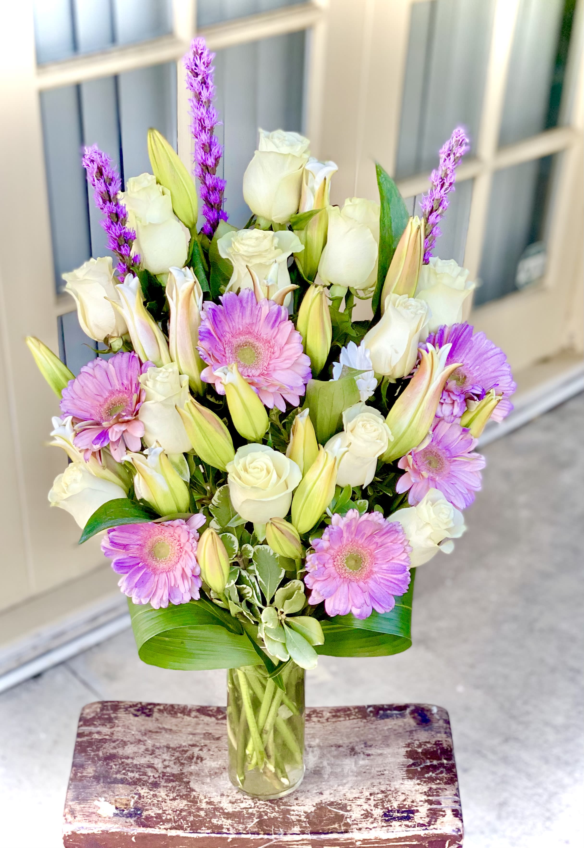 Gerbera Daisies White Roses &amp; Lily Elegant Gift Bouquet  - Send an elegant gift today! This gift bouquet  is created with fresh white roses, white lilies and lavender gerbera daisies arranged in a  classic glass cylinder vase; vase measures 9"H 