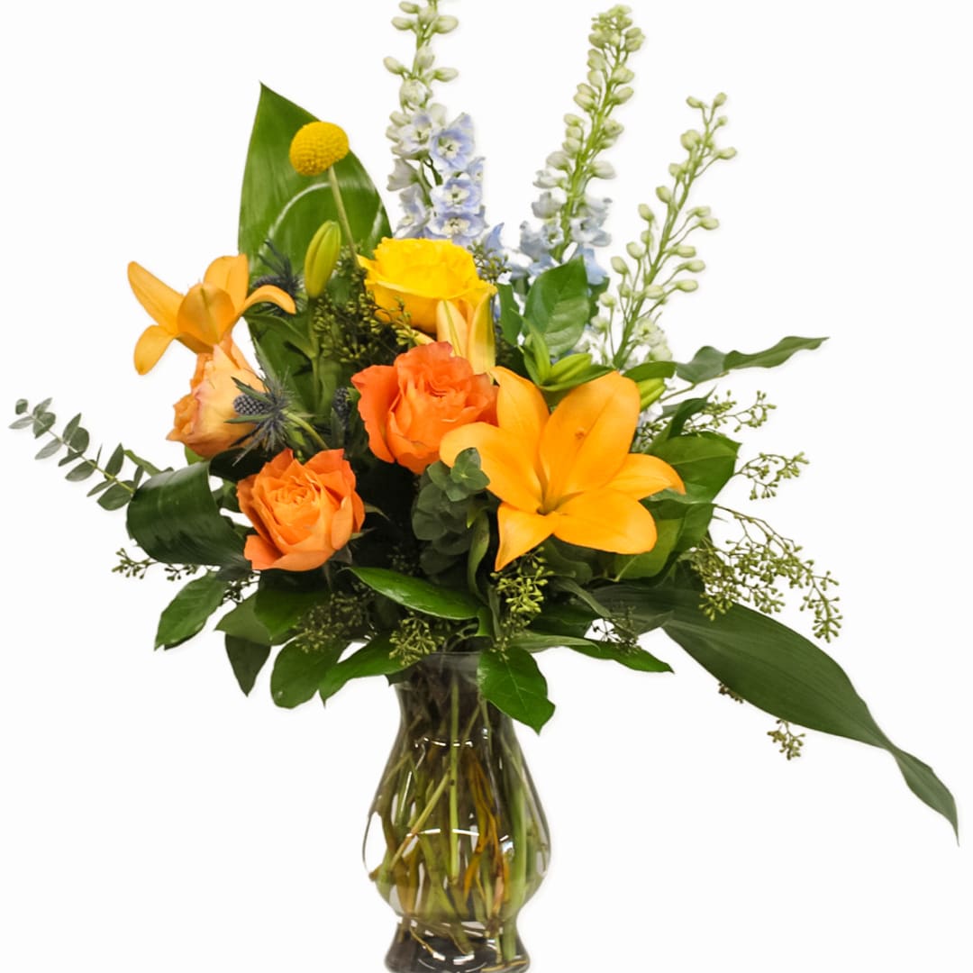Sunrise  - This colorful arrangement includes a variety of orange and yellow hues. Neatly designed with  orange and yellow roses, orange lilies, blue delphinium, blue thistle, yellow crespedia, seeded and spiral eucalyptus, with a touch of tropical foliage. whether you're looking to brighten someone's day, or just to say thank you, this arrangement will help express how you feel. 