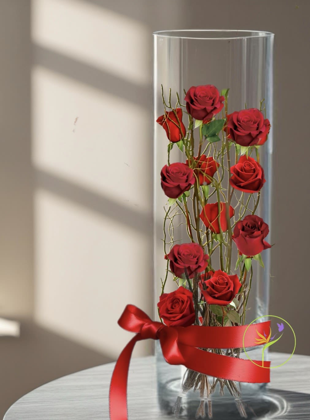 Tower Of Love. A Floral Archist™ Original. - 12 Beautiful red roses artistically designed in a 24” clear glass cylinder. Branches for structurally support. Guaranteed to impress!  Suitable for Him!  NOTE: Our flowers and greens are a gift from nature. It’s shade, depth or size might vary, design, value and aesthetic remains the same. In support of our efforts to aide in the preservation of our planet, PJf uses Fair Trade flowers, Plants, Upcycled and Recycled containers.