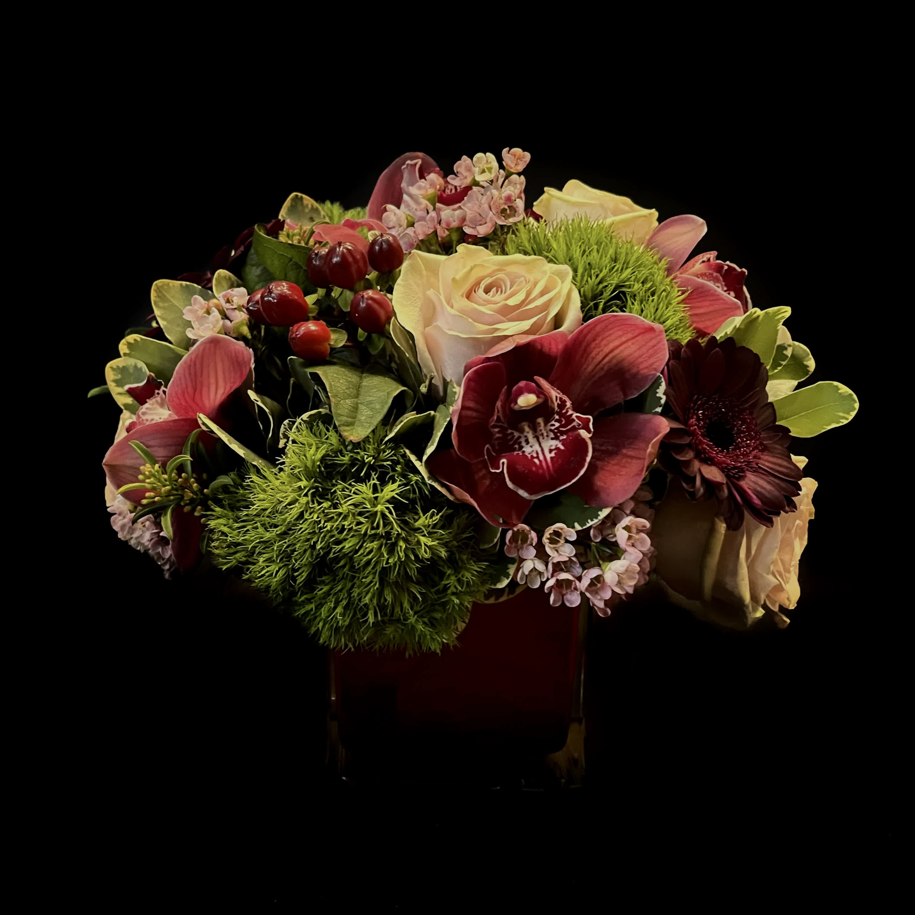 Dark and Moody - A dark arrangement of orchids, garden roses, dianthus, hypericum, dark red gerbera daisies and wax flower.