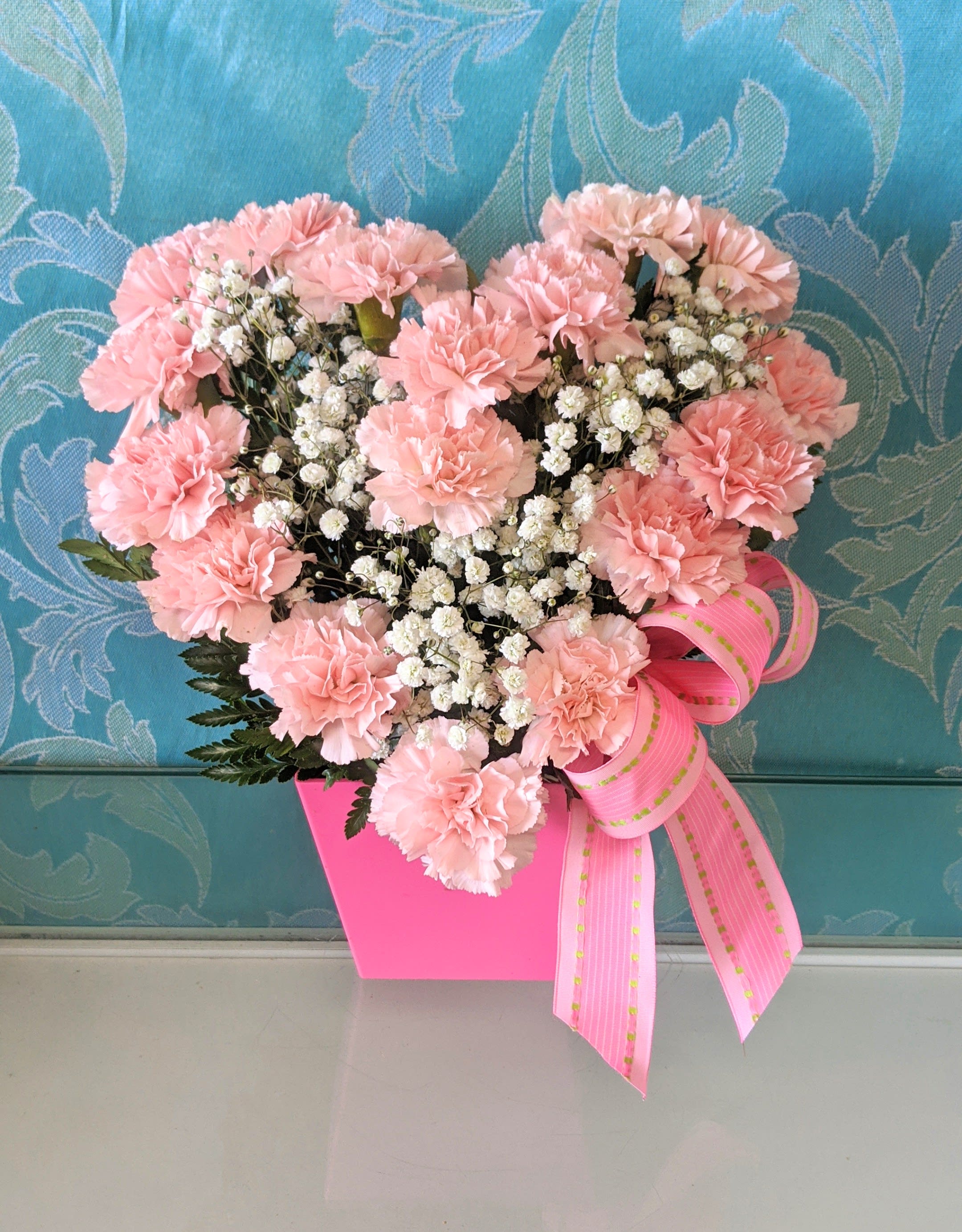 My Heart Blushes - approx. 14 pink carnations in the shape of a heart with babies breath in the center and a decorative bow in a tall pink container. carnation color may be red or dark pink if light pink is sold out.
