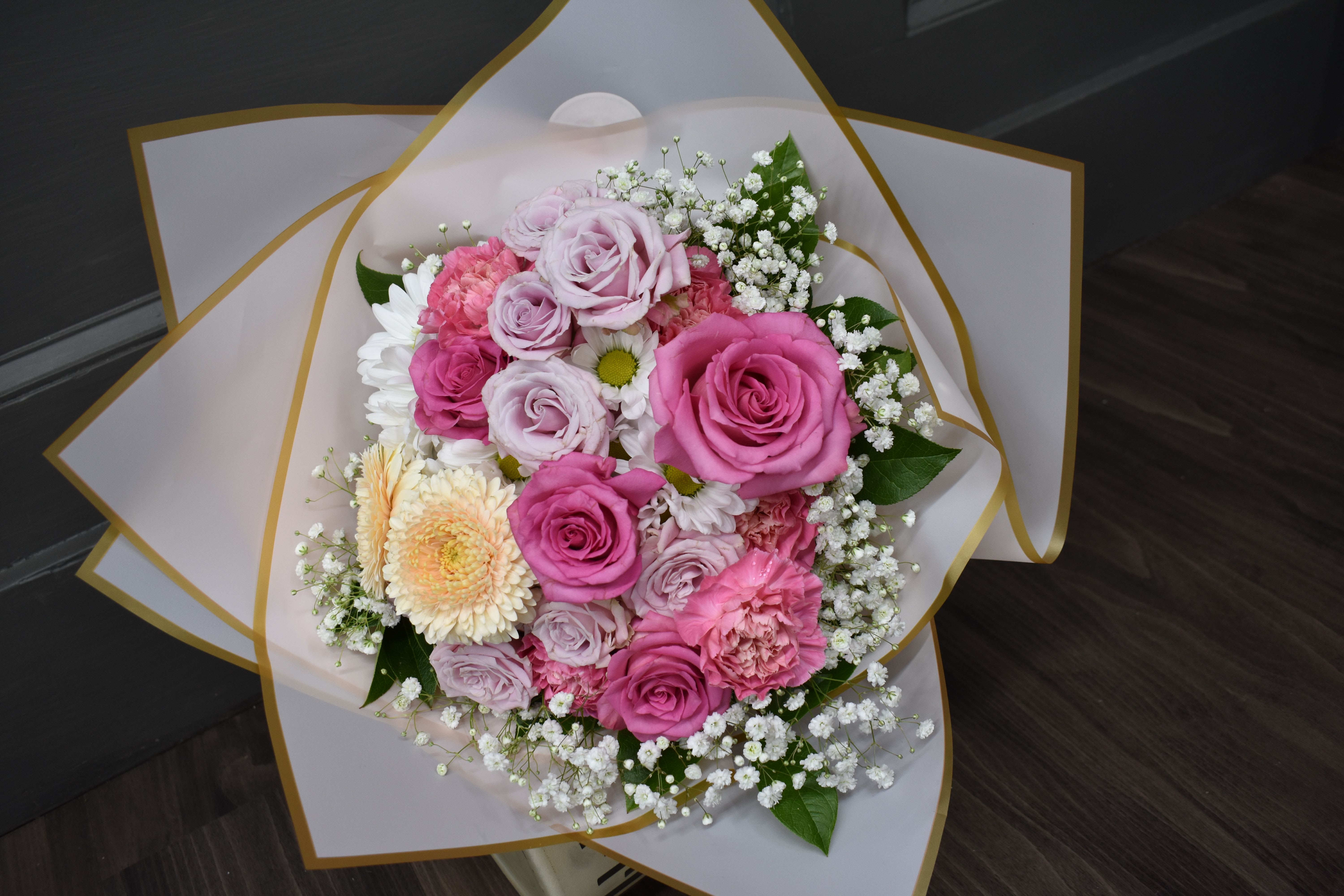 Medium Fancy Wrap Bouquet - vase not included  - Have a vase at home or want an extra special display to hand to your Valentine? Our NEW wrapped bouquet might be for you! We grouped some of our favorites, daisies, gerrondo gerbera daisies, spray roses, and roses delicately arranged with fresh greenery and baby's breath, then hand-wrapped in our gold-edged wrapping. These flowers also come wrapped with our Arrive-Alive system that covers and hydrates the stems to make sure they last until you get home. Remember to give them a fresh cut before putting them in a vase and use the flower food packet we send with!