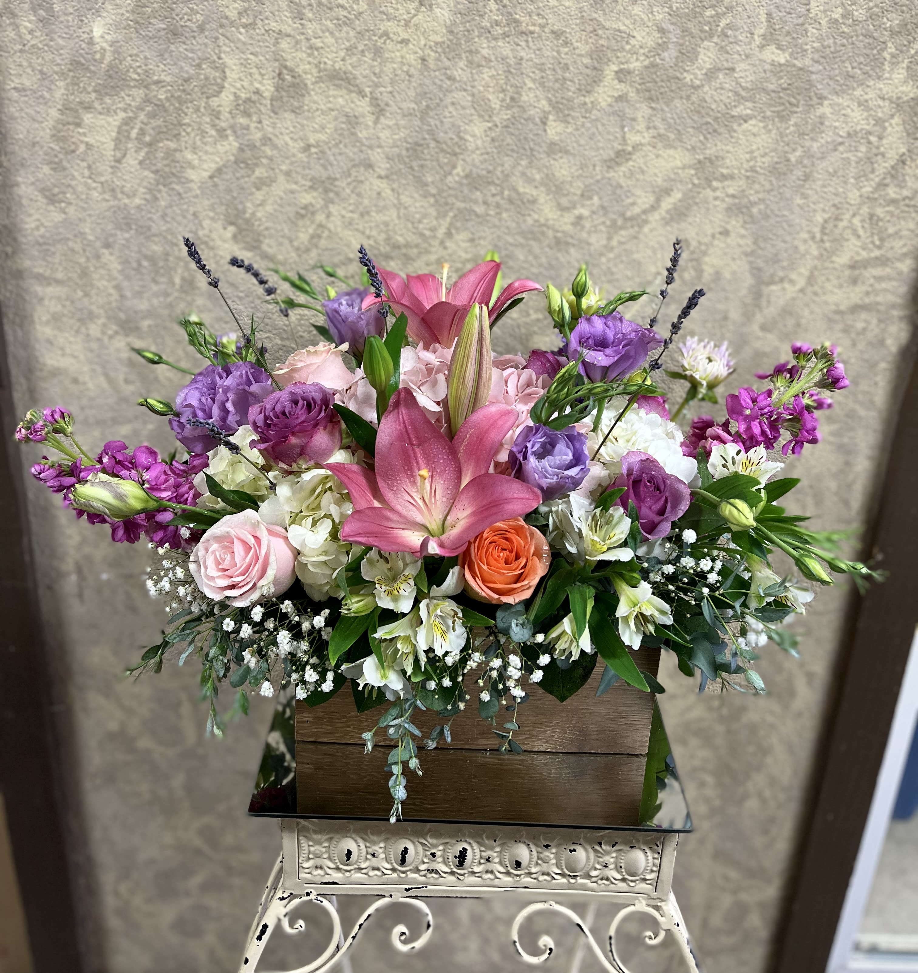 Agua Dulce, California - A sweet arrangement to celebrate someone with or a dinner party event. Recipe: Purple and Ivory Roses, Pink Asiatic Lillies, White Hydrangeas, Purple Lisianthus, White Alstroemerias, Hybrid Blue Delphiniums, and Lavender (seasonal) in a local handmade, wooden box. Seasonal: July- September Design View: All-sided Facing View Photo shown: Standard
