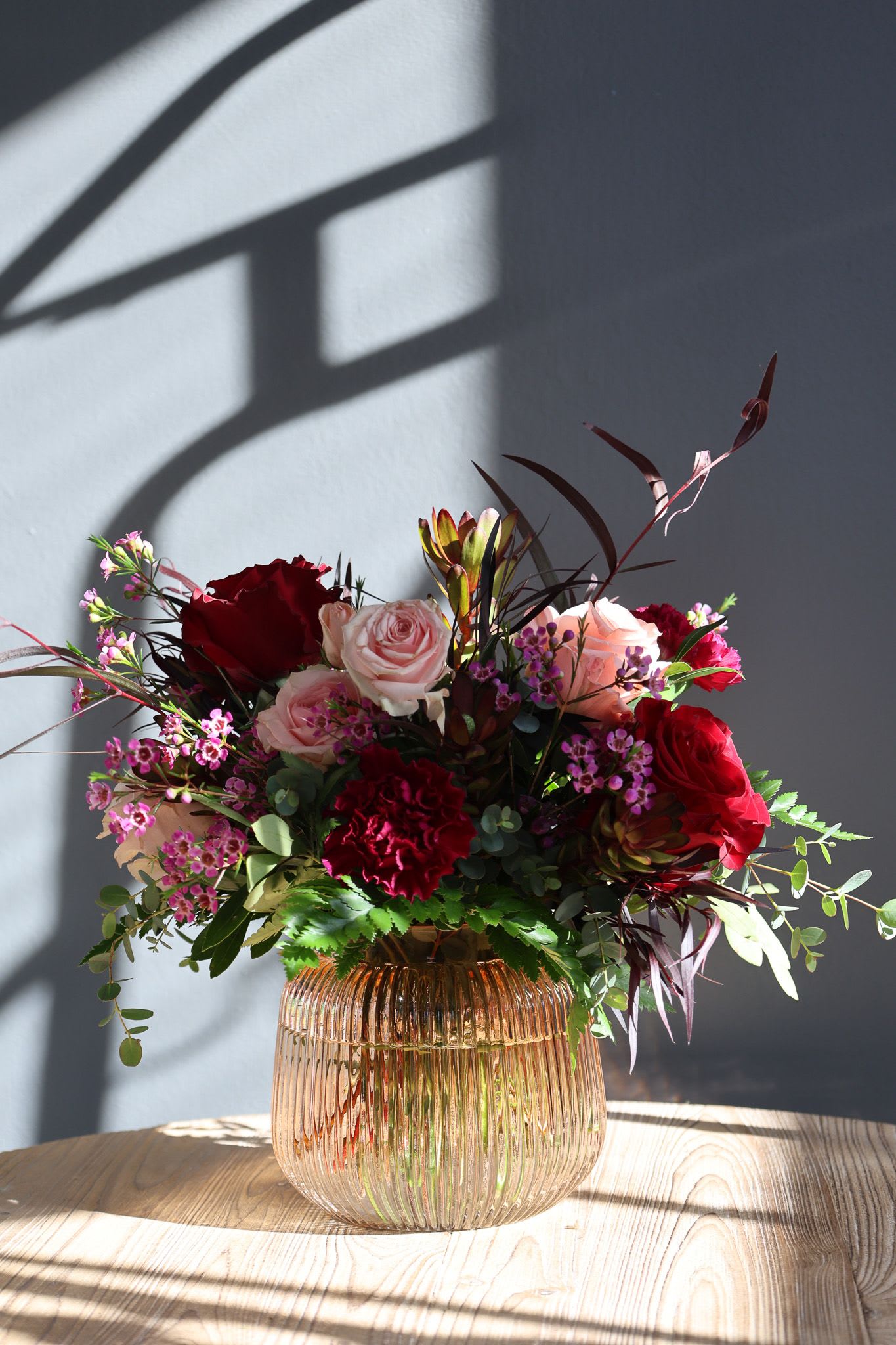 Blushing - A beautiful mix of pink and red garden roses and carnations in a beautiful blush toned ribbed keepsake vase