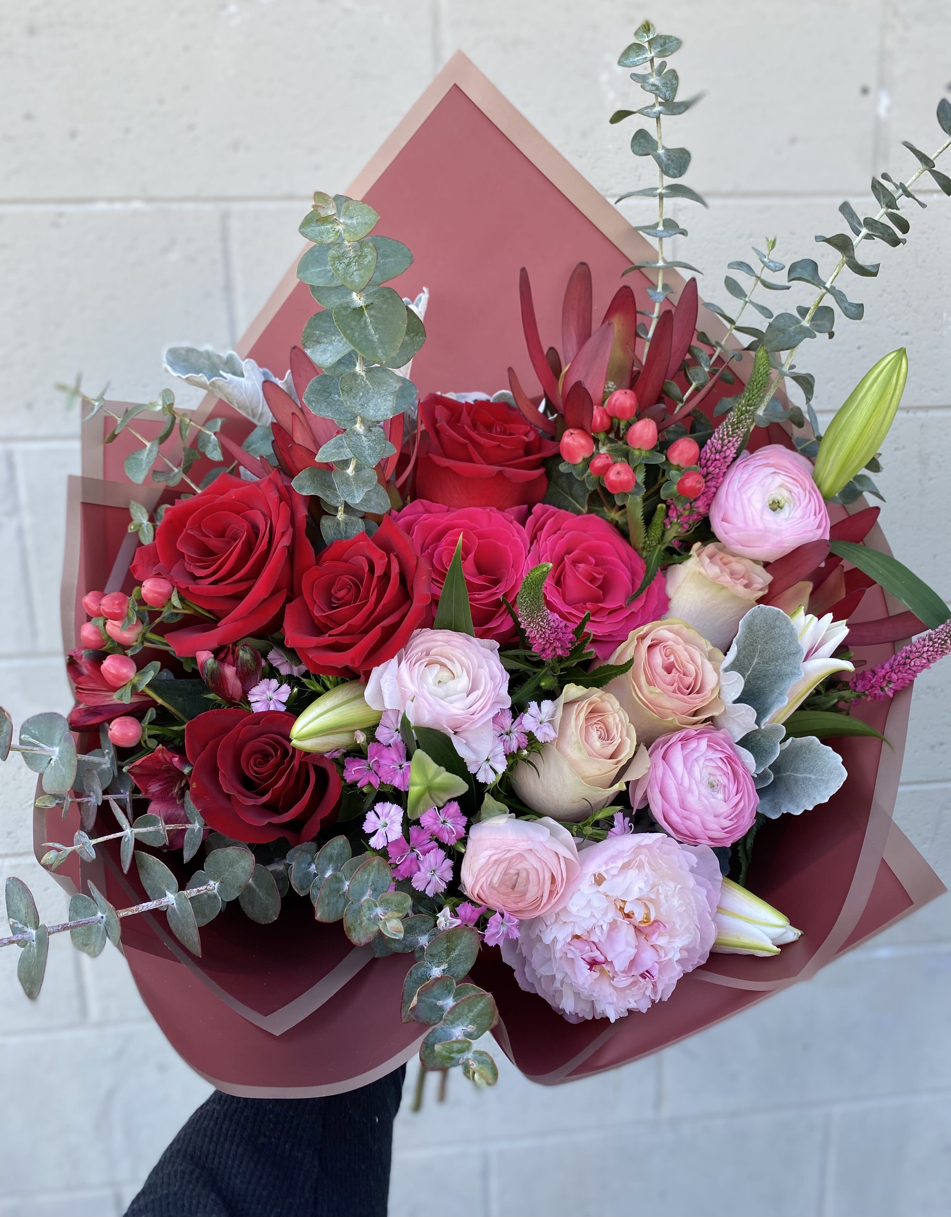 Crazy in Love - A hand-tied bouquet with an ombre look of pinks and red with roses, ranunculus, dusty miller, lilies, and peonies. 