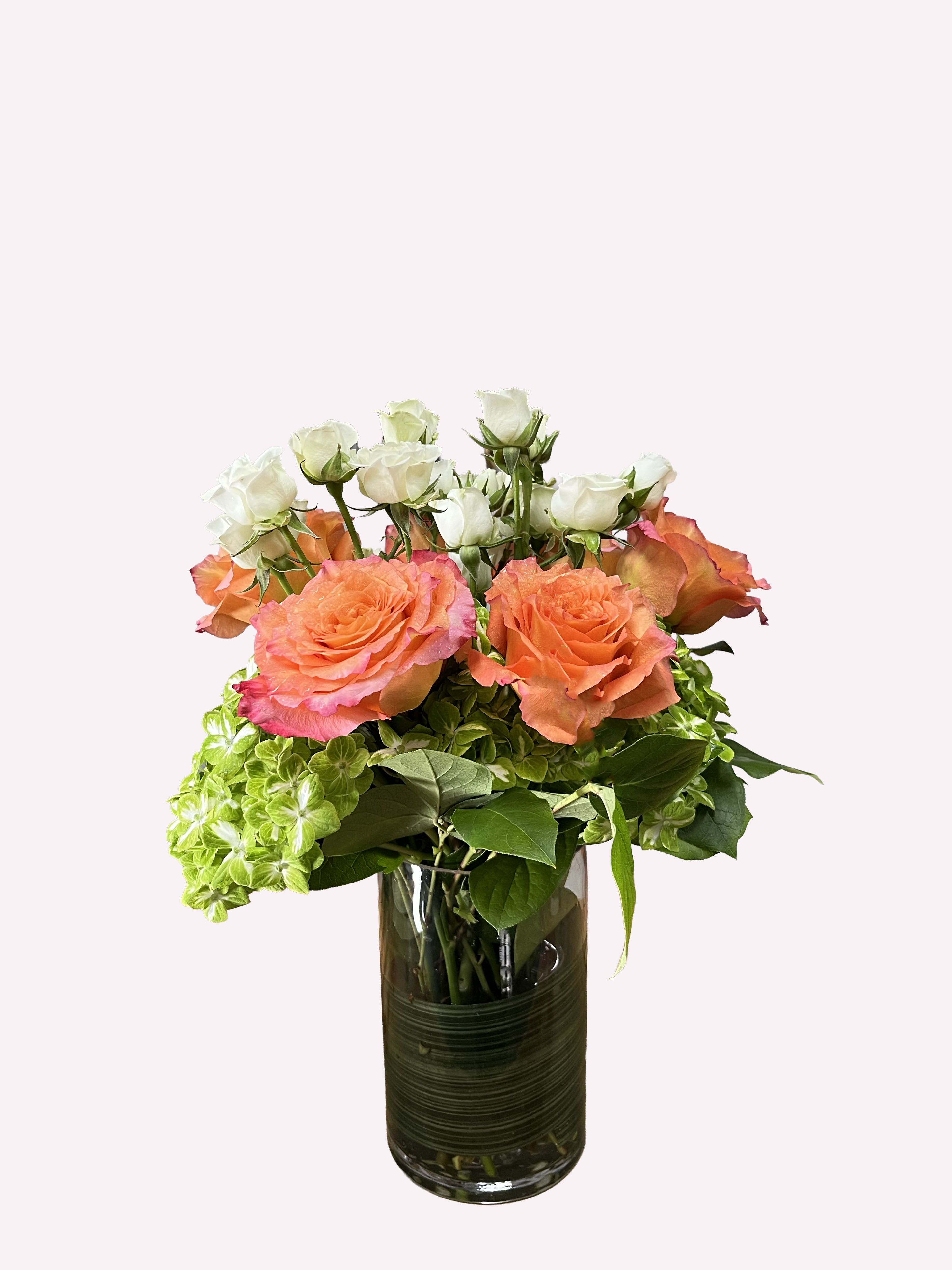 The Crown's Spirit - A delightful version of one of our most popular vase arrangements, featuring vibrant peach roses, white mini roses, and green hydrangeas, happily arranged in a glass vase.   