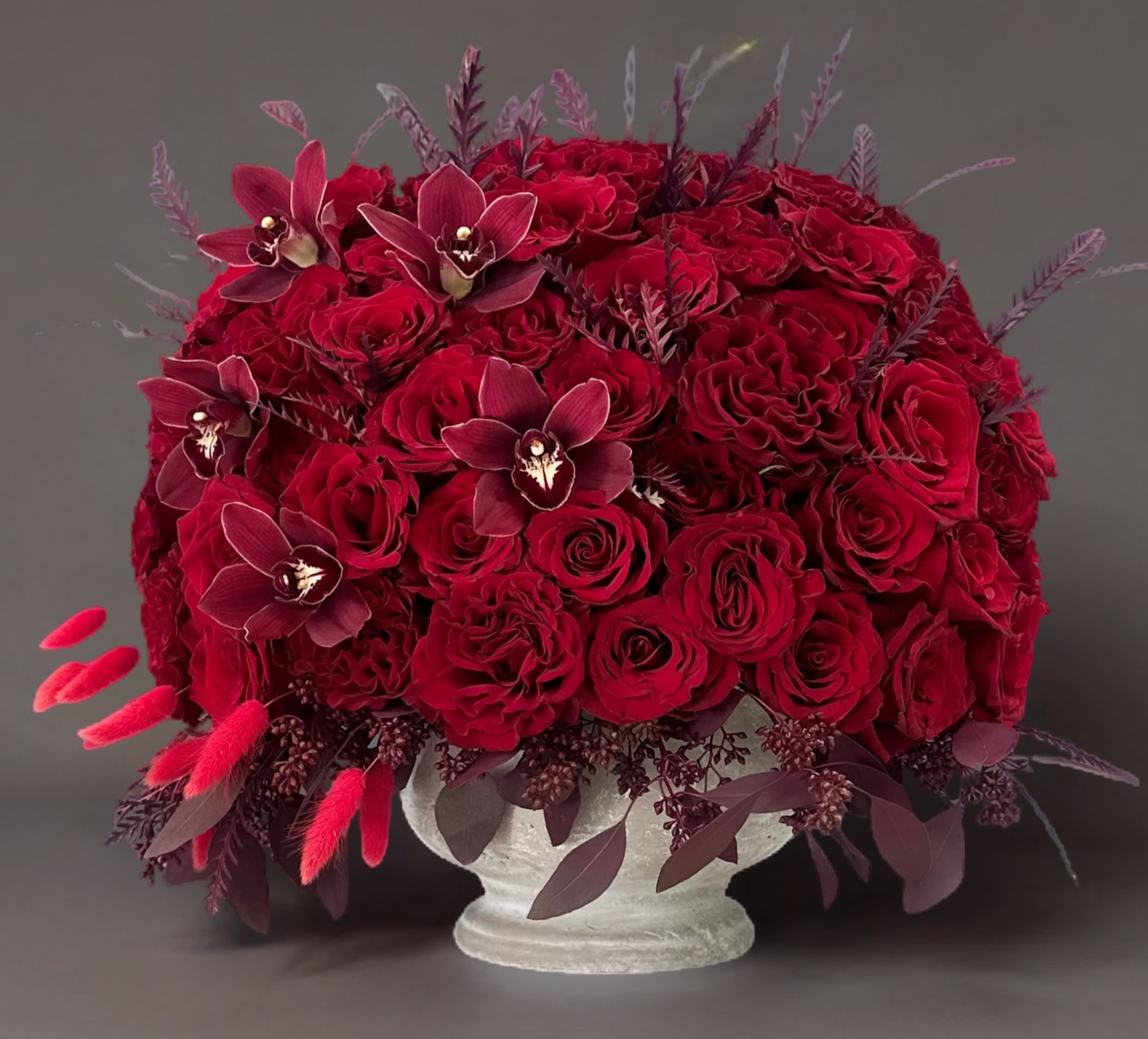 Urban Rouge Harmony - The rich, red hues of the roses evoke feelings of love and desire, while the cement vase adds an element of modernity and understated elegance. The raw, natural charm of the cement vessel complements the classic beauty of the roses, making this arrangement a captivating focal point in any space.  As the roses gracefully unfurl, they reveal their intricate layers, creating a visual masterpiece that captivates the senses. This arrangement is not merely a display of flowers; it is a celebration of love, sophistication, and the enduring beauty found in the perfect union of nature and craftsmanship. Place it in your home or gift it to someone special to add a touch of romance and contemporary charm to any setting.