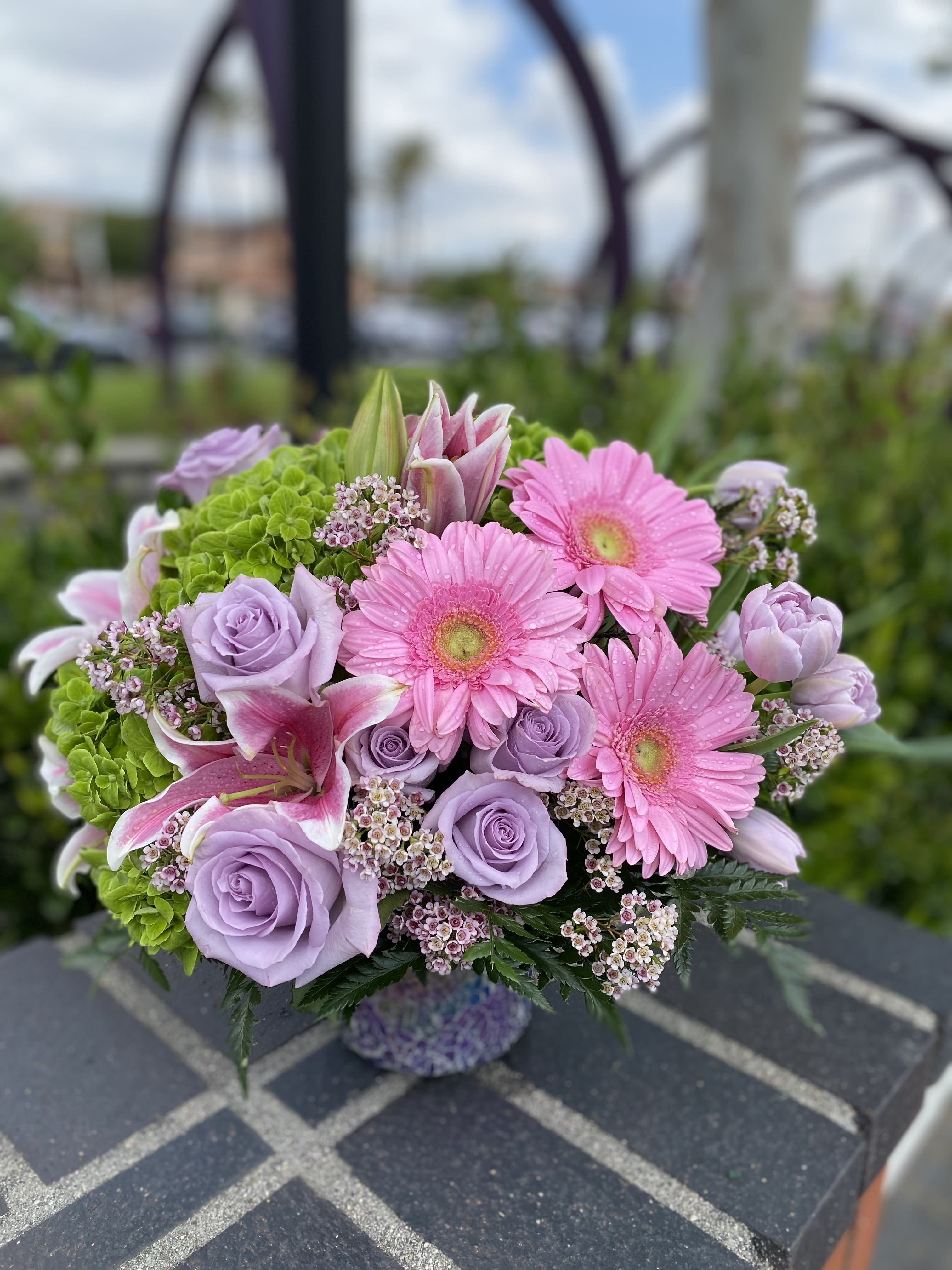 Whisper of Romance - A profusion of purple, pink, lavender and green blooms such as roses, tulips, gerbera, hydrangea and much more are and hand Delivered in a purple Shining Beauty cylinder.  Add more roses deluxe price for pic up we are next to 85 degrees  Add more stargazer lilies and Roses Premium 