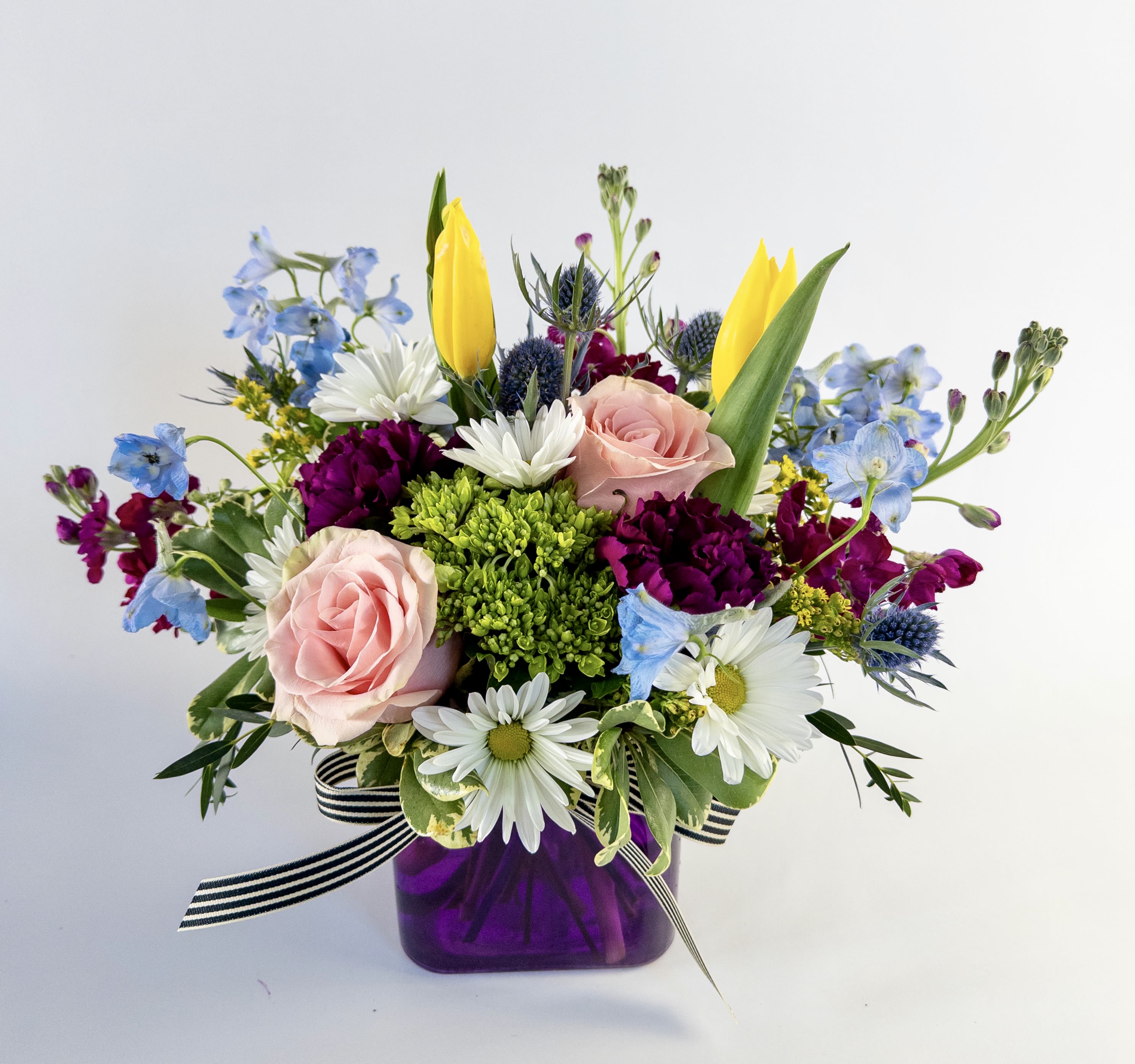 Spring Garden Cube  - A colorful mix of fresh flowers in a colored cube vase. Mix may vary but will be in the pink, purple, blues and yellow shades. Bright and colorful for the winter blues and a reminder spring is on the way. 