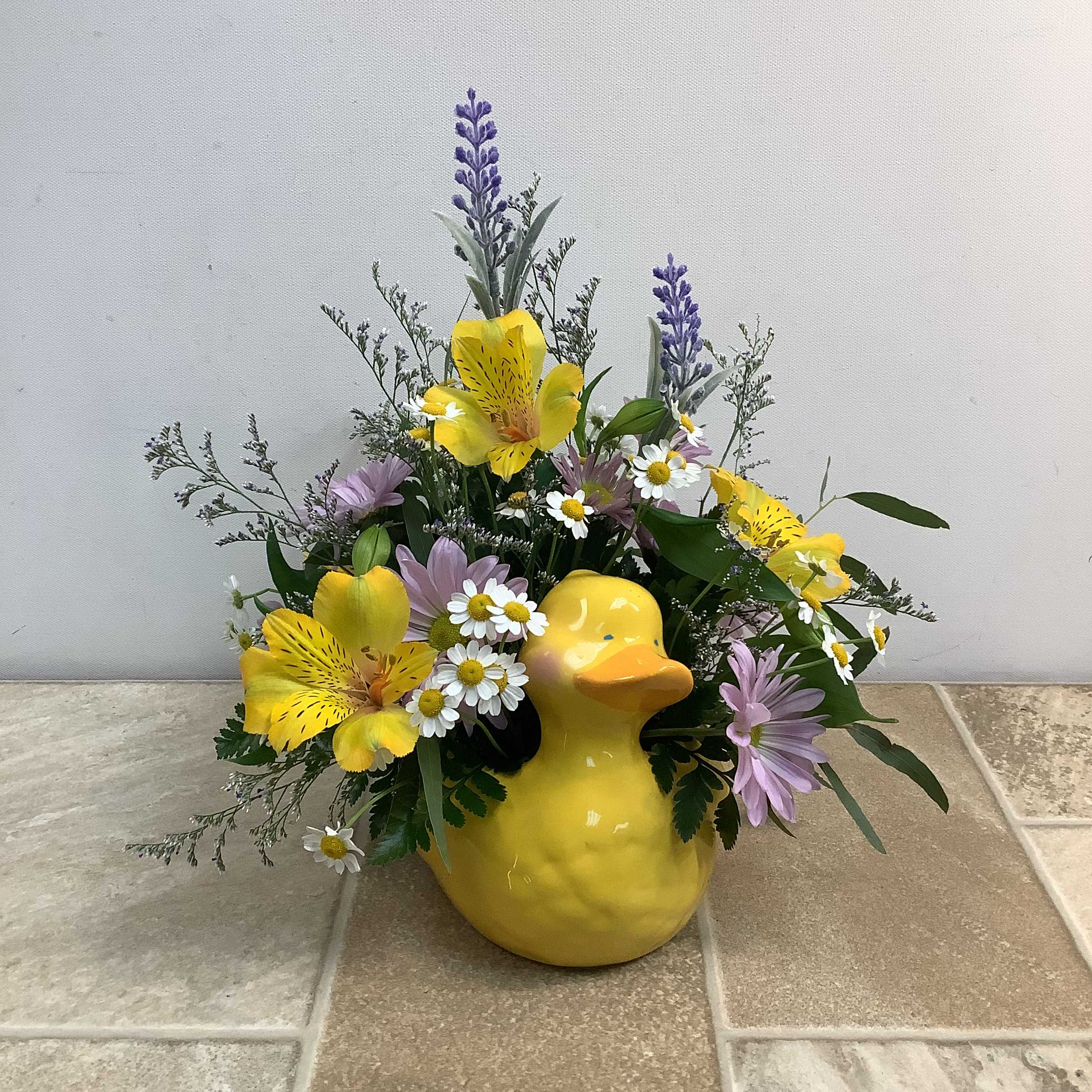Just Ducky - Sure to bring a smile, this delightful bouquet is arranged in a friendly ceramic duck. The cheerful collection of fresh blooms includes bright yellow alstroemeria, soft lavender daisies, delicate white and yellow feverfew, and blue limon accents. Assorted foliage adds depth and texture.  