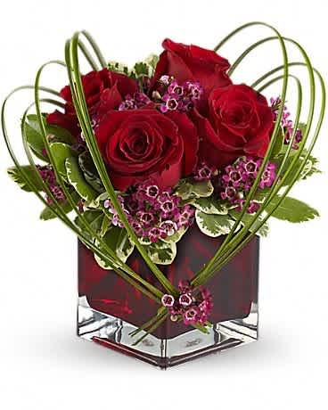 Teleflora's Sweet Thoughts Bouquet with Red Roses - If you'd like someone to think sweet thoughts about you, send them this delightful bouquet! A graceful heart of bear grass is tied with purple waxflower, and appears to float above red roses nestled in a ruby-red glass vase. How sweet it is! Red roses and purple waxflower accented with variegated pittosporum and bear grass arrive in a Teleflora red glass cube vase.