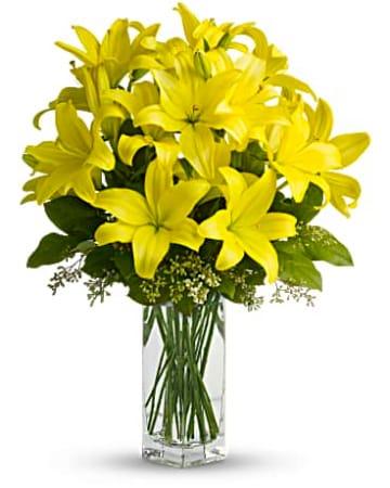LILY SUNSHINE  - A bright and elegant display of yellow lilies arranged with fresh mixed greenery in a clear glass vase, offering a cheerful touch to any space. 