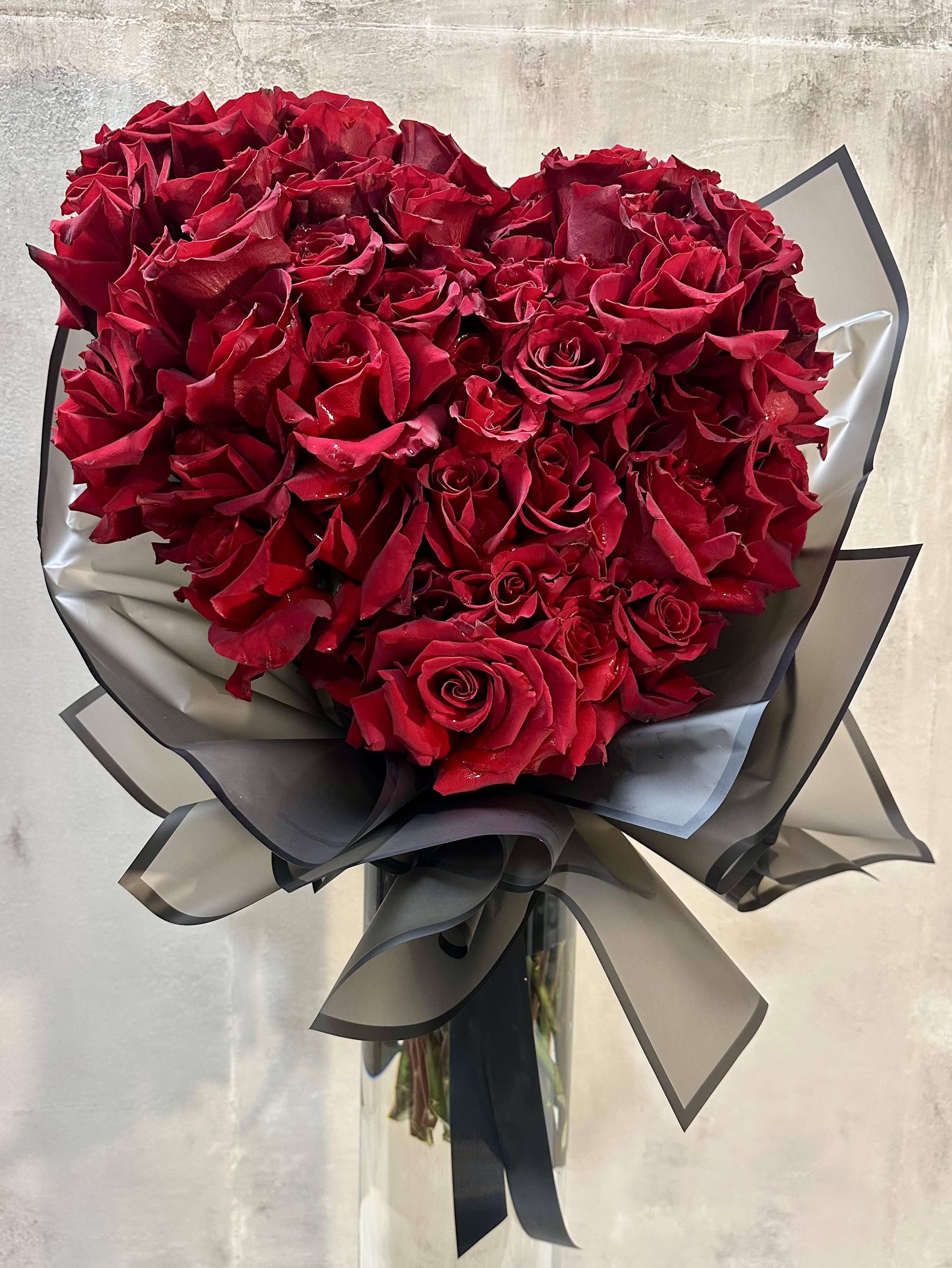Heart of Roses Handtie Bouquet - A breathtaking statement of love, handcrafted entirely from 40-50 premium red roses arranged in a lush, sculptural heart. Wrapped in elegant, modern layers and finished with a dramatic ribbon detail, this design is timeless, romantic, and unapologetically grand. This is a handtie wrapped in paper with a wet wrap ** NO VASE