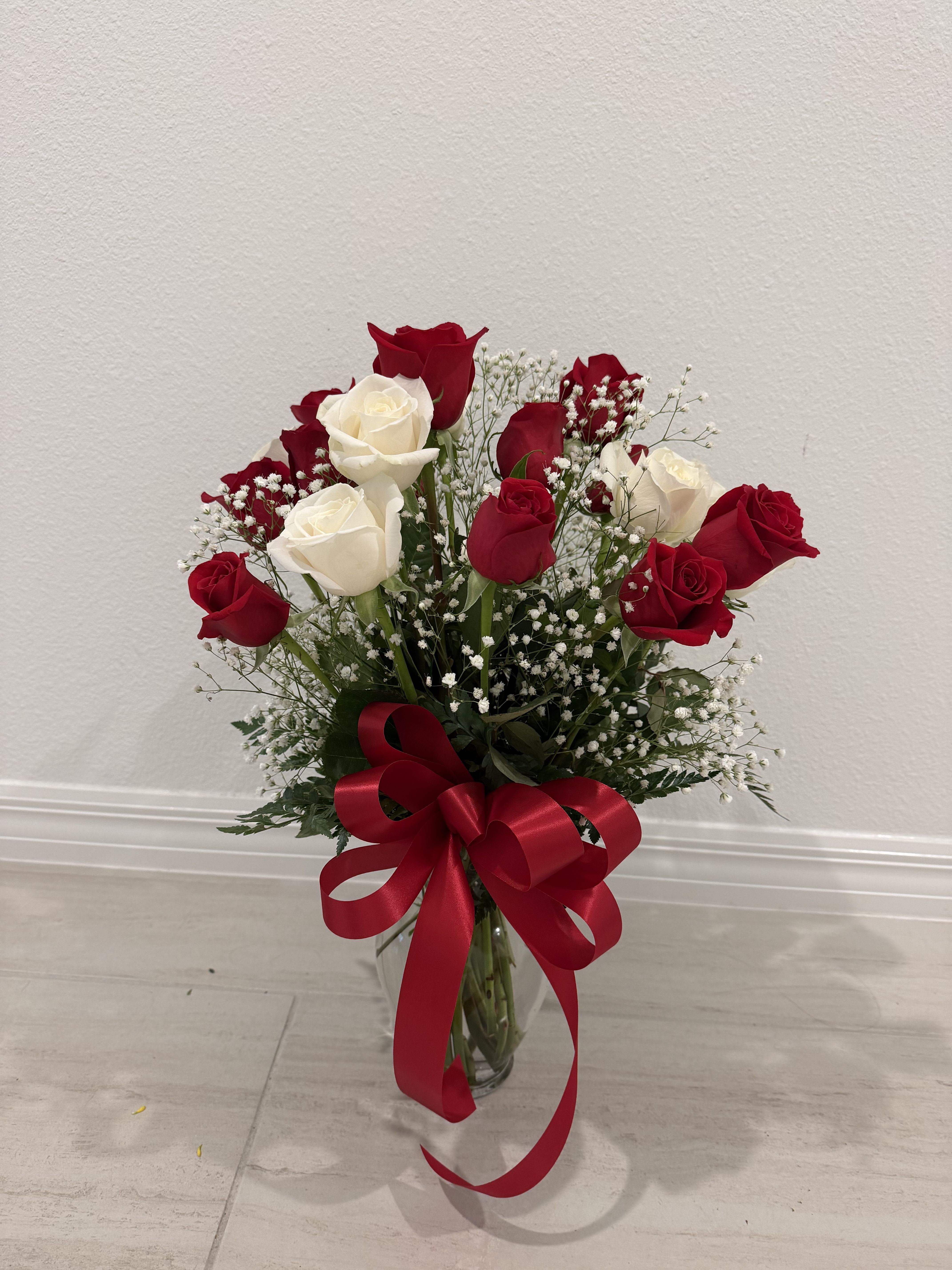 Timeless Red &amp; White Rose Vase - A graceful arrangement of fresh red and white roses, artfully accented with delicate white baby’s breath and lush greenery. Presented in a clear glass vase and finished with a bold red satin bow, this timeless floral design beautifully expresses love, respect, and heartfelt sentiments—perfect for anniversaries, Valentine’s Day, or any meaningful occasion.