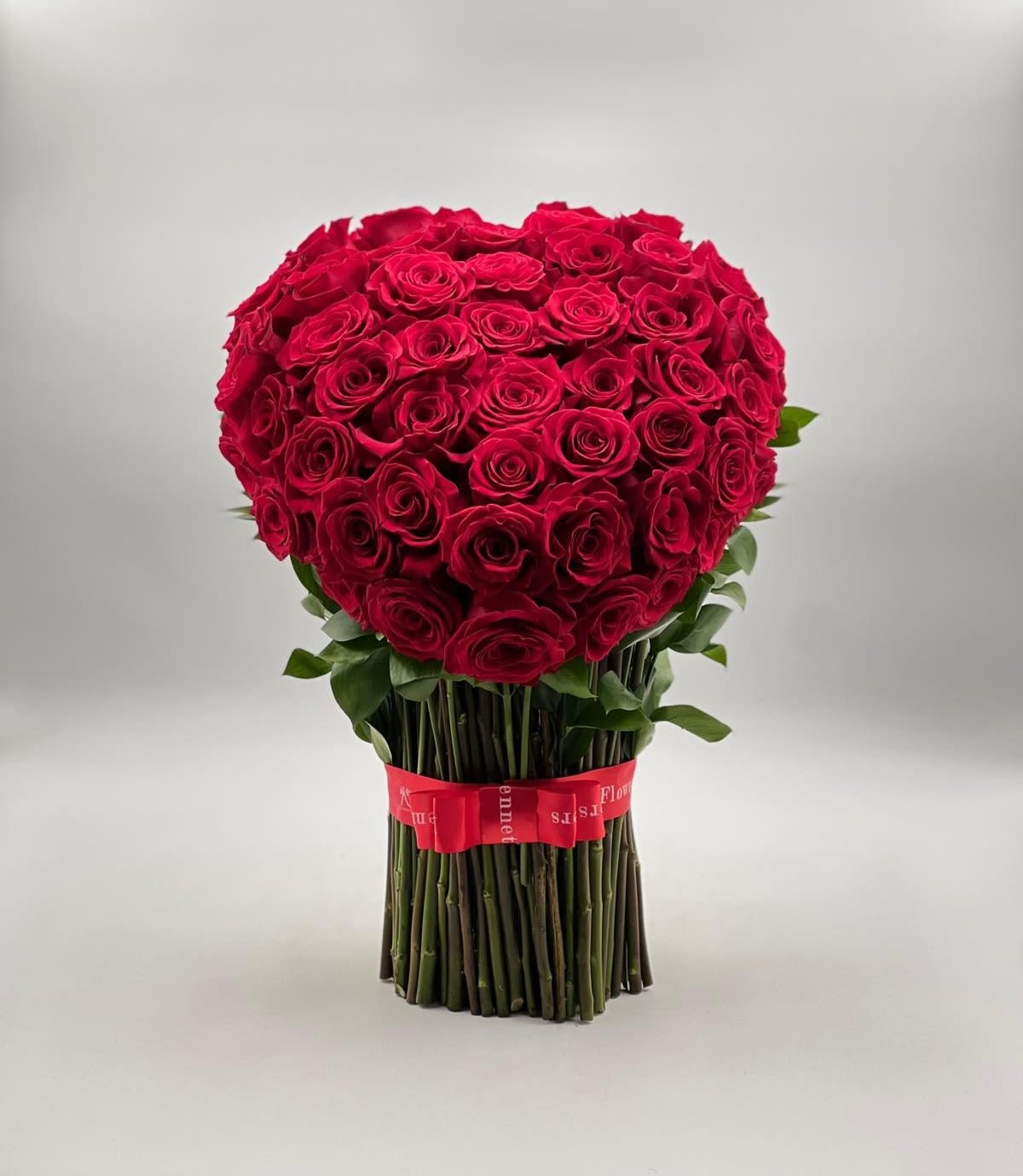 Valentine’s Royal Heart - This arrangement is a breathtaking statement of love, featuring dozens of perfectly arranged red roses shaped into a full, luxurious heart. The blooms are tightly clustered to create a rich, velvety texture, while the clean vertical stems wrapped with a red ribbon add a refined, modern touch. Elegant, bold, and undeniably romantic, this piece is designed to leave a lasting impression and express deep passion in the most timeless way.