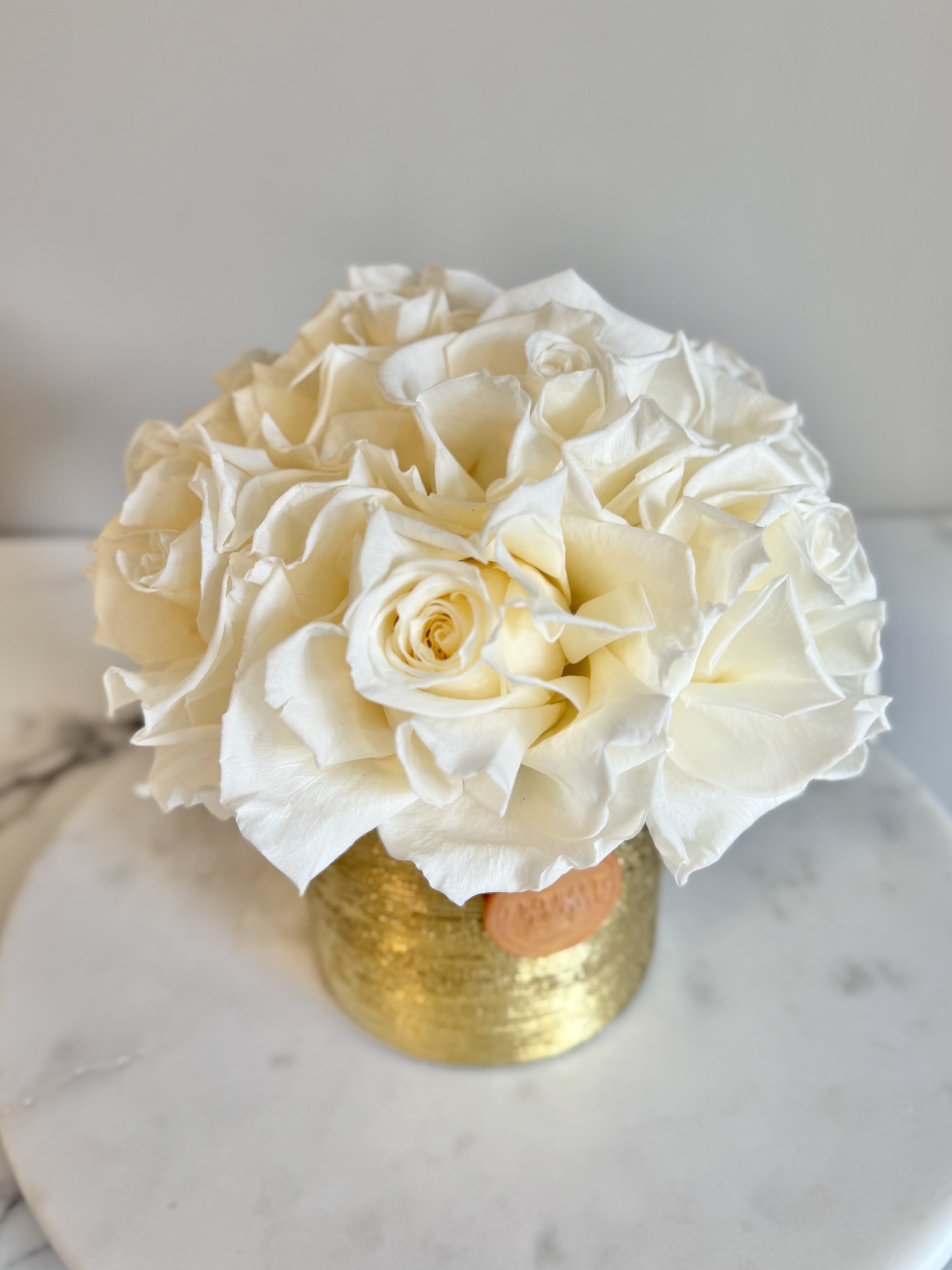 Eternelle Pearl - Gold Petite - A timeless treasure in bloom. Eternelle Pearl features eight exquisite pearl-white preserved roses, artfully arranged in a lustrous gold vessel. Radiating quiet luxury and purity, this piece is designed to make a statement—elegant, enduring, and effortlessly graceful. Perfect as a thoughtful gift or a sophisticated accent for any space.  Lasting beauty that never fades—just like the moments it’s meant to celebrate.