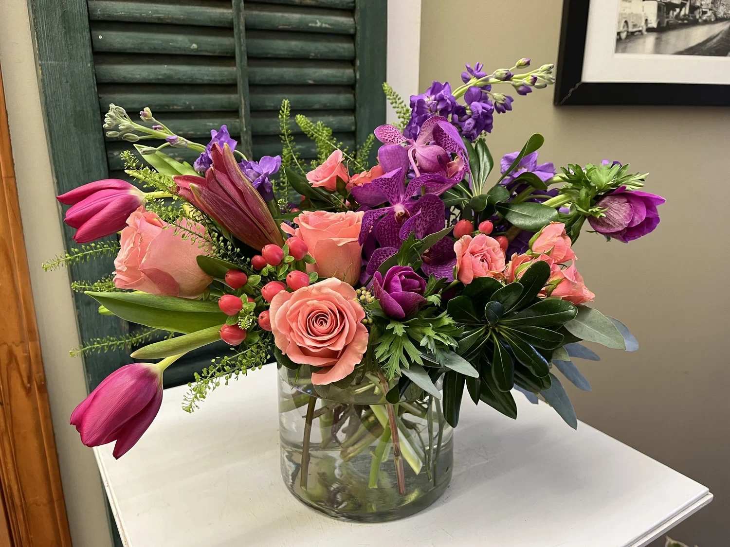 And I Love Her - A bold arrangement of jewel toned flowers made in a low glass cylinder vase.
