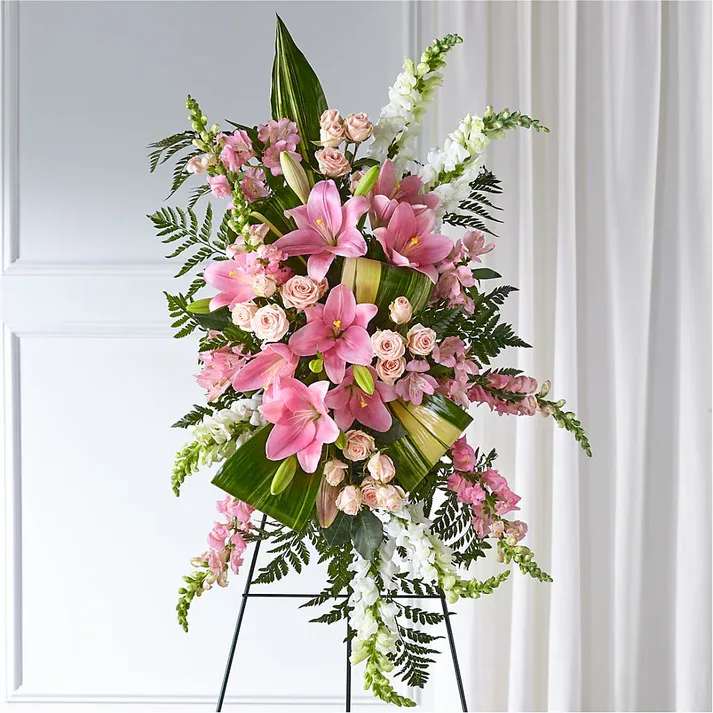 Elegant Embrace Standing Spray - Our Elegant Embrace Standing Spray shares the warmth and comfort your loved ones need during this difficult time through each blushing bloom. A local florist beautifully combines lilies, spray roses and snapdragons with greens to express your heartfelt love.  Details Approximately 38" L x 22" W