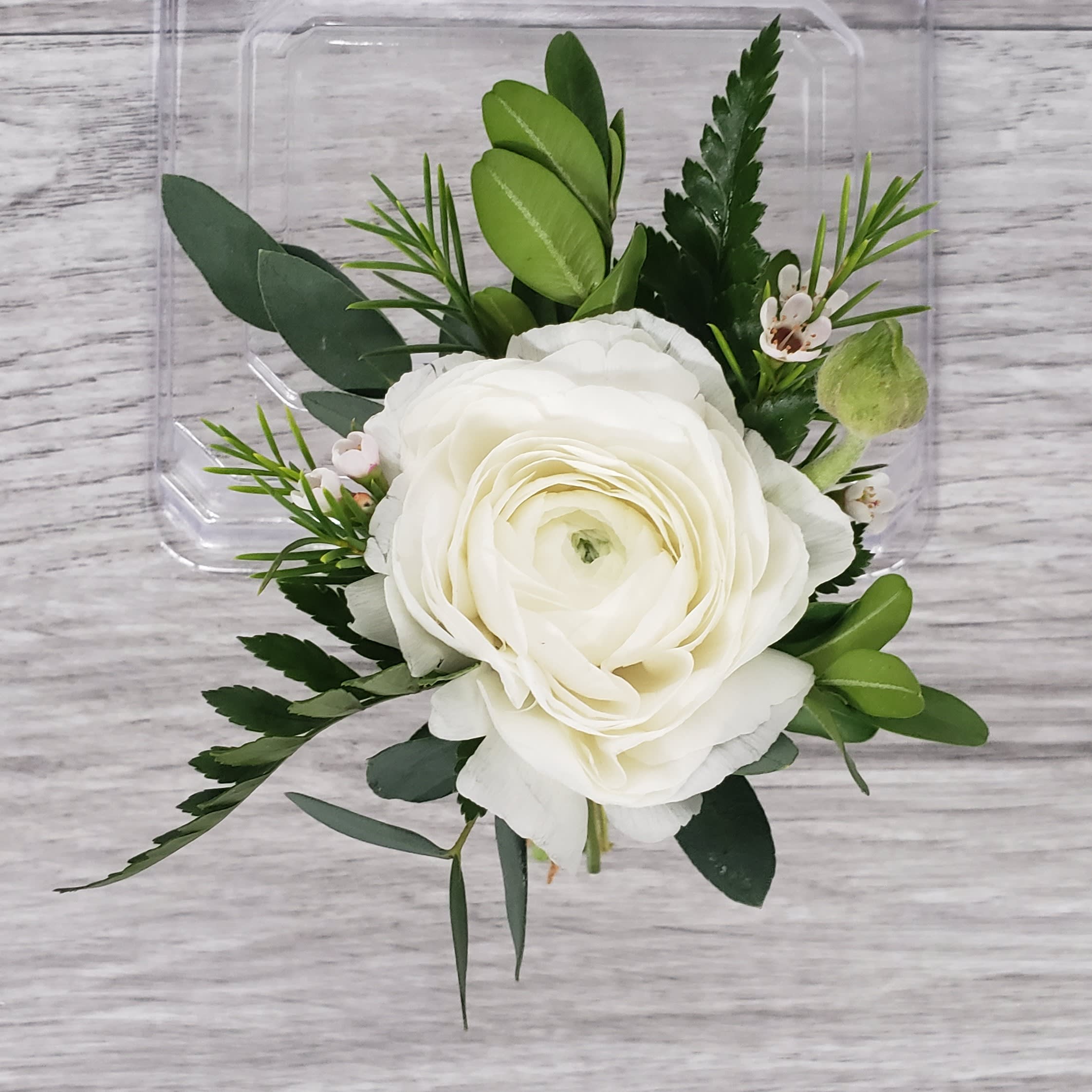 White Ranunculus Boutonniere - This Boutonniere features a white ranunculus with accent flowers and greenery. If you would like to exchange the colors of the flowers or ribbon please let us know and we will be happy to accommodate.