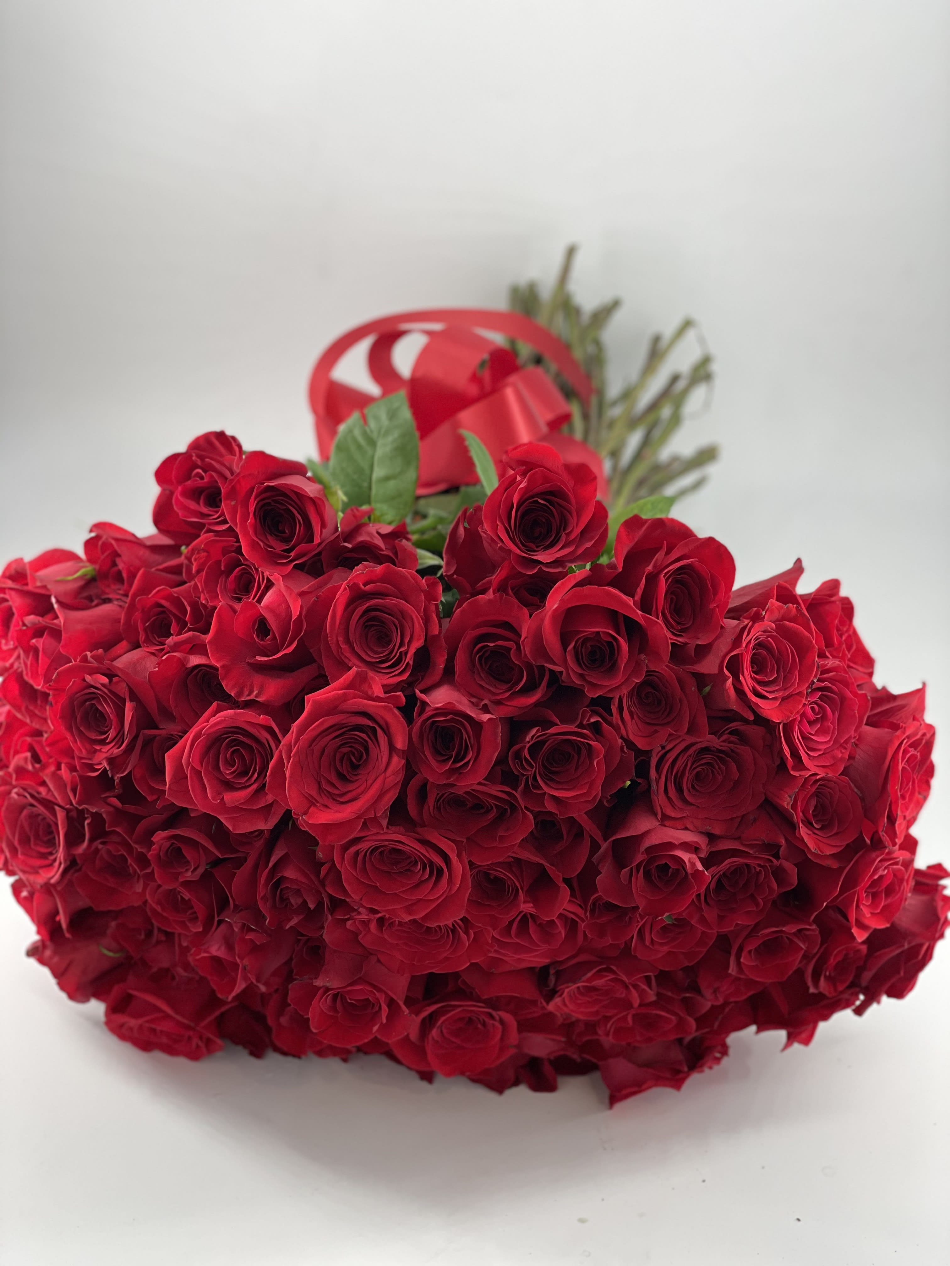 Red Indulgence - This bouquet stands second to none. Dozens of roses stunningly arranged to create the most luxurious bouquet. A red ribbon bow completes gives it perfect touch. The recipient is sure to be the envy of onlookers. *Other Rose colors available upon request.  This arrangement comes with a accompanying vase.