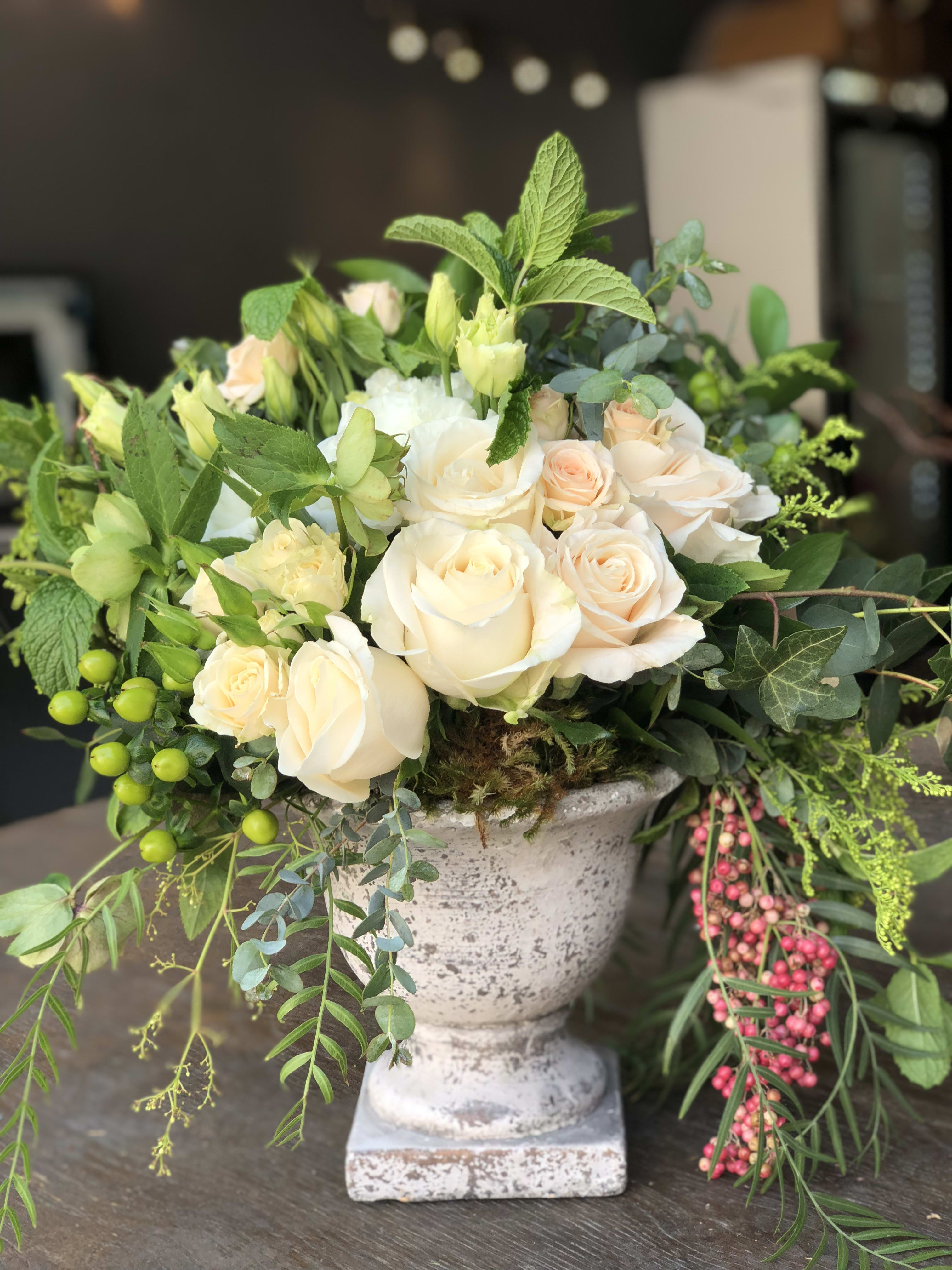 Mama Carina - Bring the essence of a garden into any home with this exquisite design. White roses, spray roses, freshly cut mint, freesia, and more are artfully arranged in a stone sanctuary urn. This arrangement not only enhances the beauty of any space but also fills the air with a refreshing floral fragrance. Ideal for adding a touch of natural elegance to your home decor or gifting to someone special. Order now to elevate your surroundings with this timeless and aromatic floral arrangement!