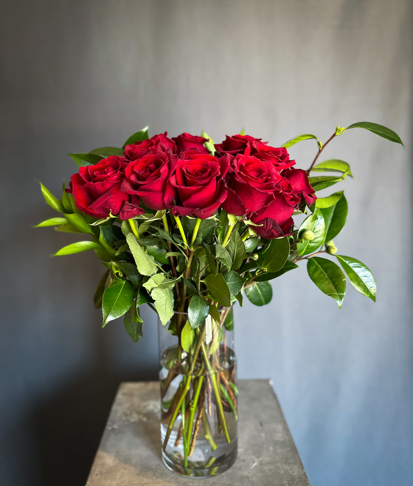 Dozzine di Rose (One Dozen Red Roses) - Say "I Love You" with an elevated touch on a classic design. This arrangement features 12 gorgeous red roses elegantly arranged in a luxurious glass cylinder  with fresh magnolia leaves. Perfect for expressing love and romance with timeless elegance. Order now for quick and reliable delivery in all of Los Angeles!