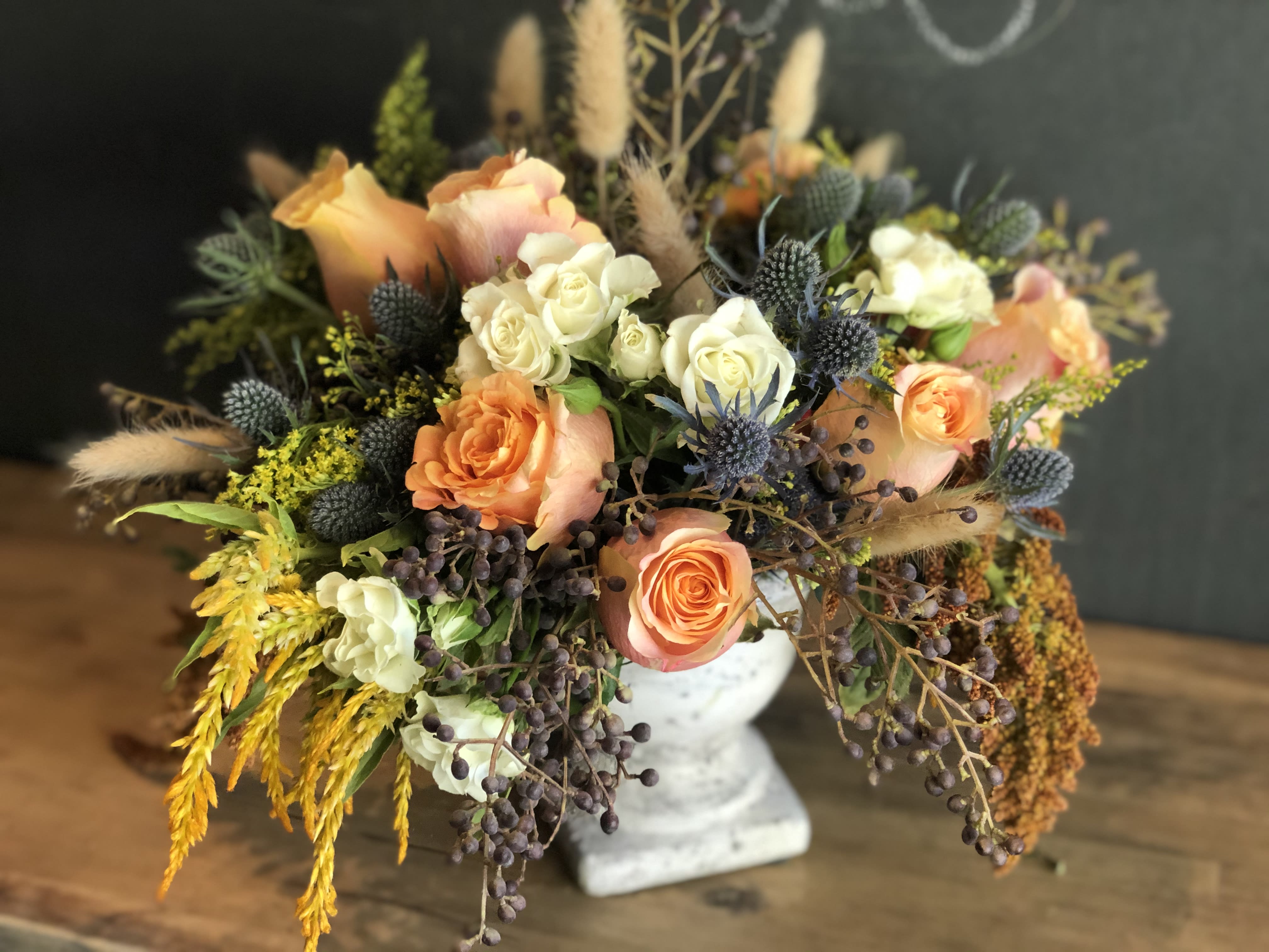 Raggio di Sole ("Ray of Sunshine") - Raggio di Sole, or "Ray of Sunshine," will brighten your day with vibrant seasonal blooms. This stunning arrangement includes Orange Crush roses, white spray roses, amaranth, thistle, and so much more, all beautifully arranged in a gorgeous cement urn. Perfect for adding a cheerful and radiant touch to any space. Order now for quick and reliable delivery!