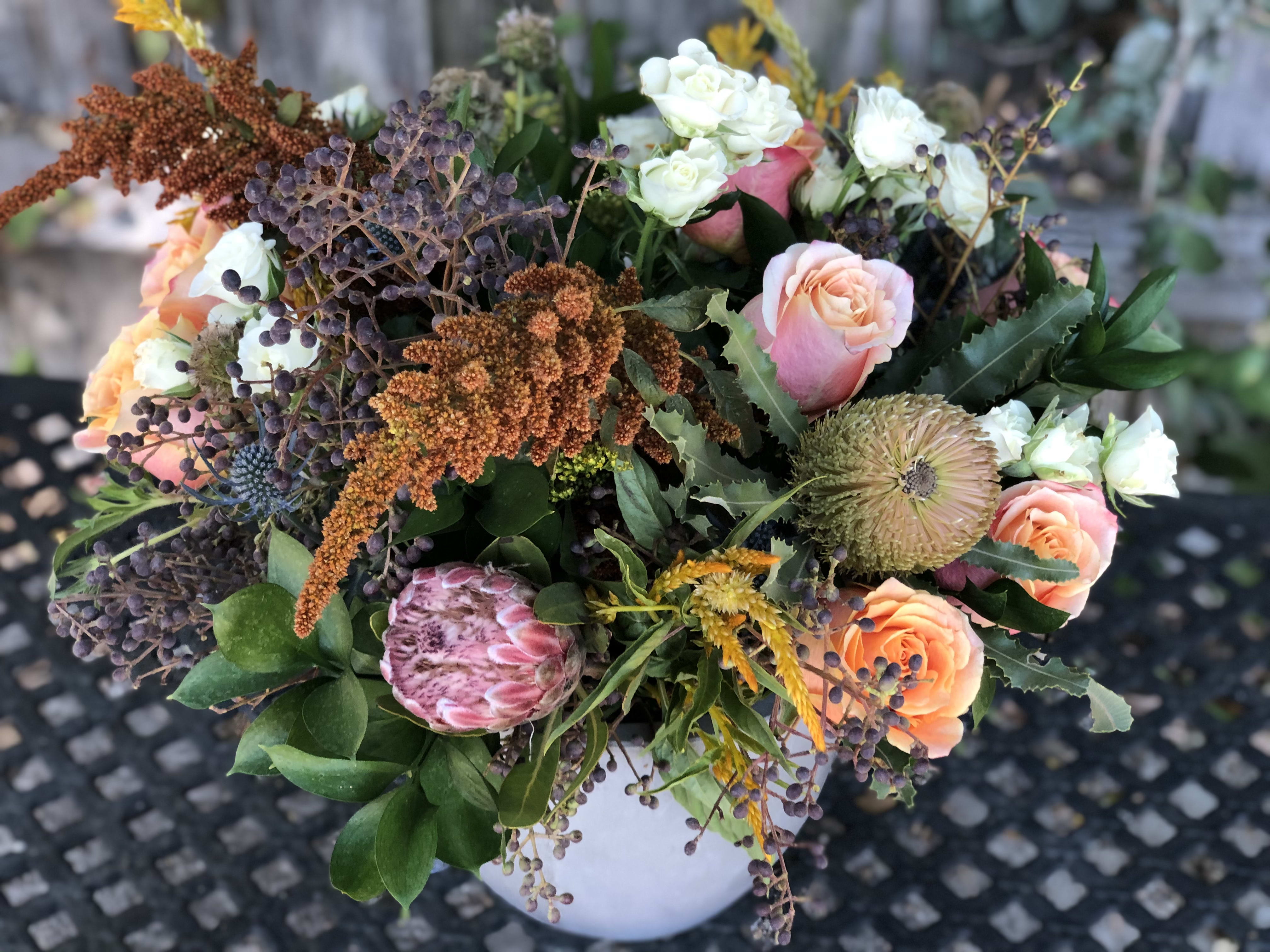 Fioriture Moderne - Impress and delight with Fioriture Moderne, a breathtaking arrangement featuring a stunning selection of seasonal blooms. From vibrant pin cushions and majestic king protea to aromatic sage and mint, alongside elegant amaranth and two-toned roses, this arrangement exudes sophistication and natural beauty. All elegantly presented in a luxurious cement bowl, it makes a striking centerpiece for any setting, whether at home or in an office. Perfect for surprising someone special or adding a touch of luxury to your own space. Order now and experience the timeless elegance of Fioriture Moderne.