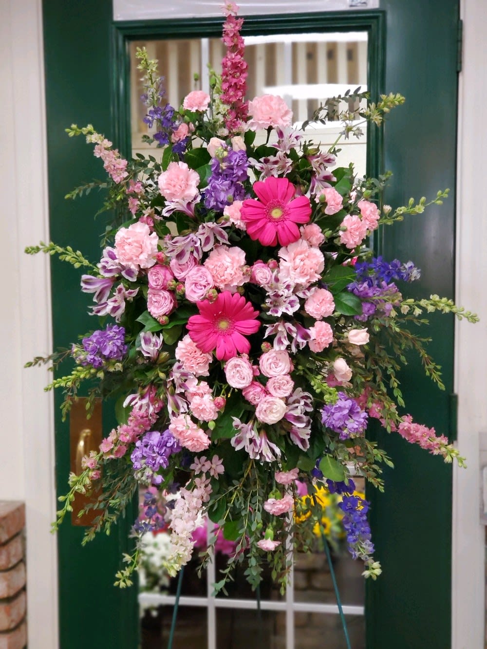 Free Spirit Standing Spray  - Standing spray on an easel with gerbers, spray roses, carnations, stock, larkspur and alstroemeria