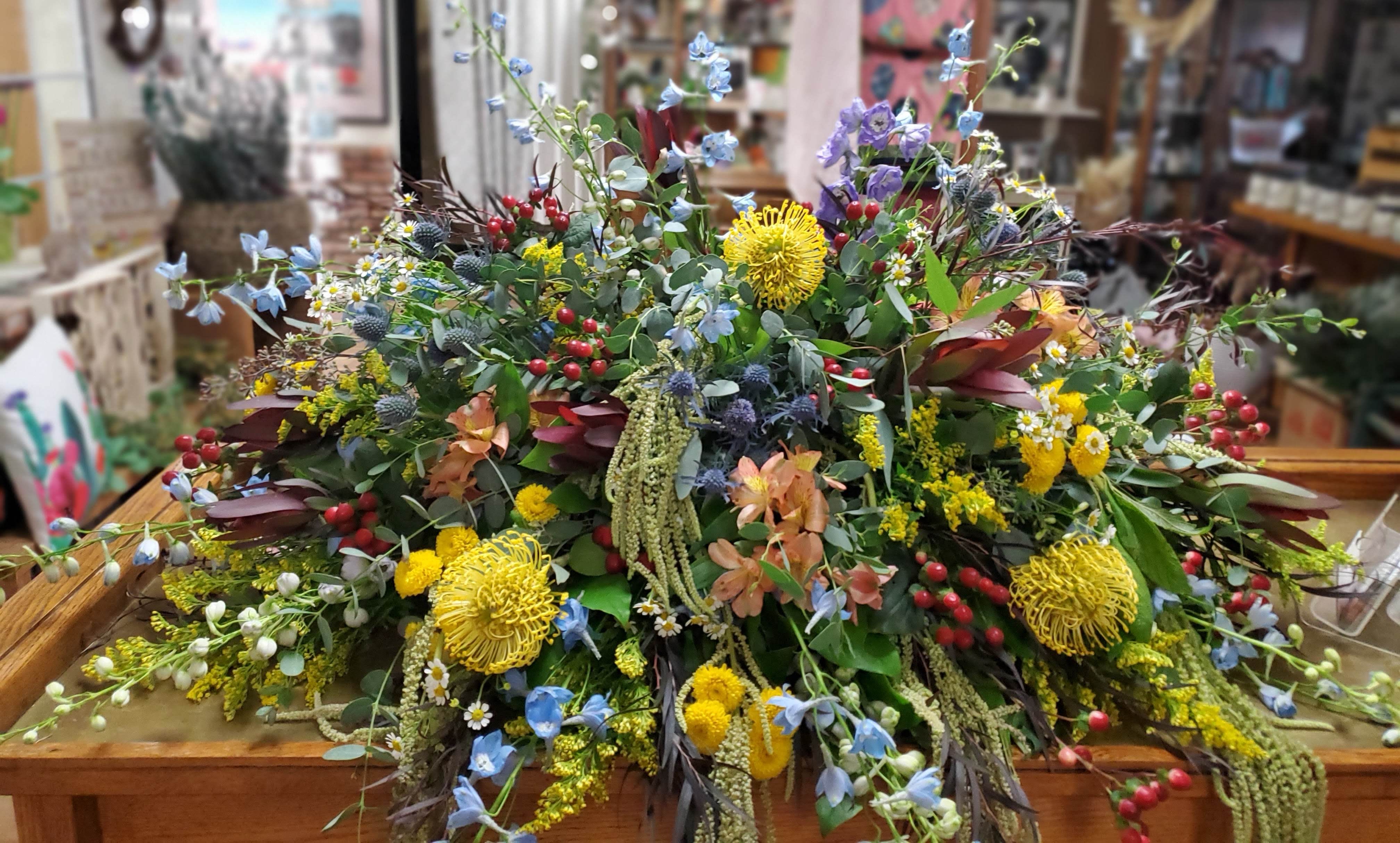 Wild &amp; Free Casket Piece  - Half casket piece to include pincushion protea, thistle, safari sunset, delphinium, hanging amaranthus, buttons &amp; alstroemeria accented with eucalyptus.