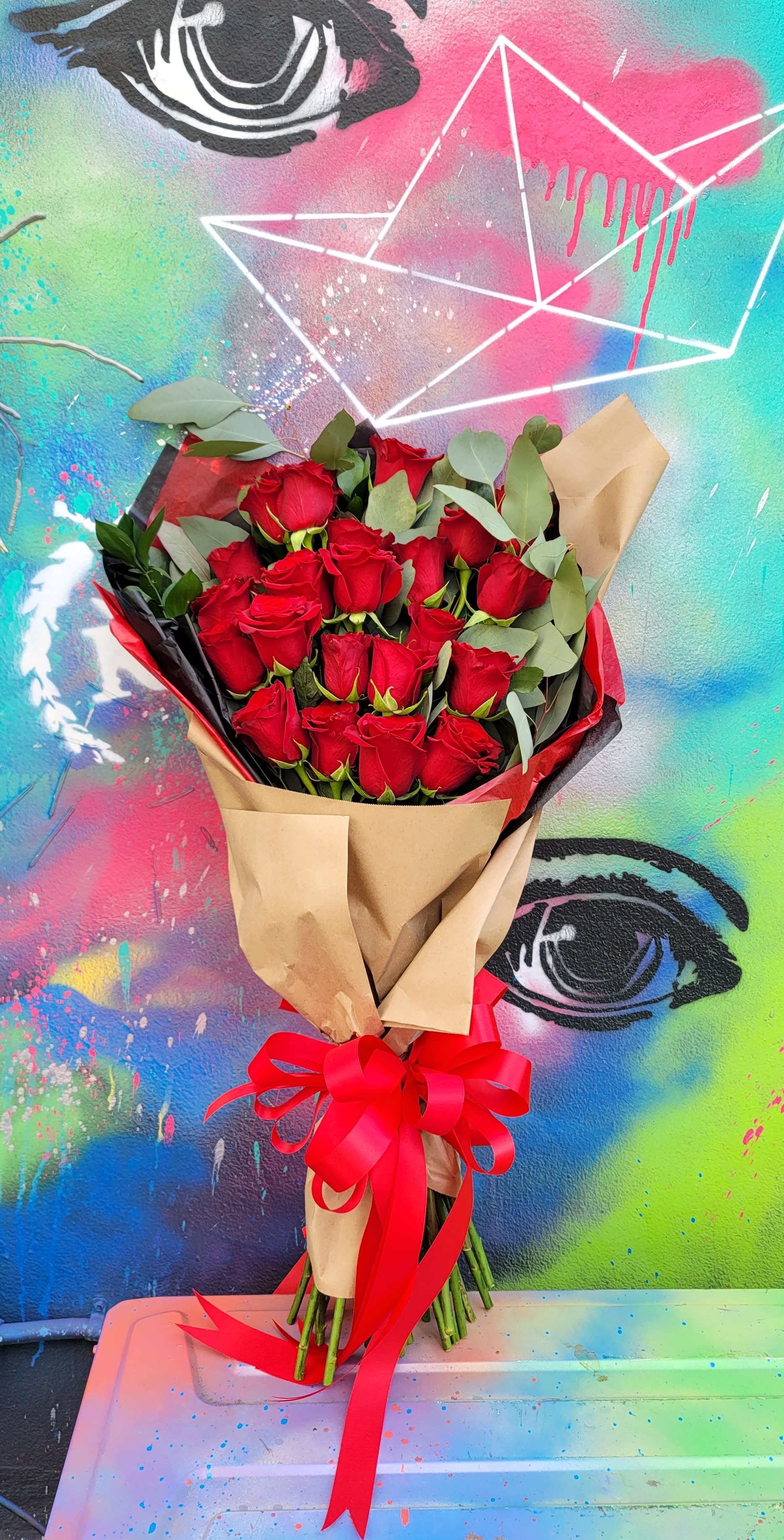 Red Roses Bouquet with Bow  - Bouquet of 18 roses with eucalyptus, greenery wrapped with craft paper, colored tissue paper, and a red bow.  The bouquet could include roses of a different color. Please specify if you want them to be a different color than red.